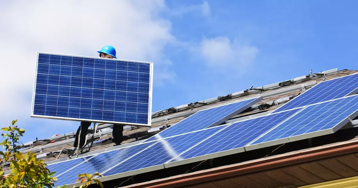 Professional solar panel installer lifting a panel into place during rooftop installation