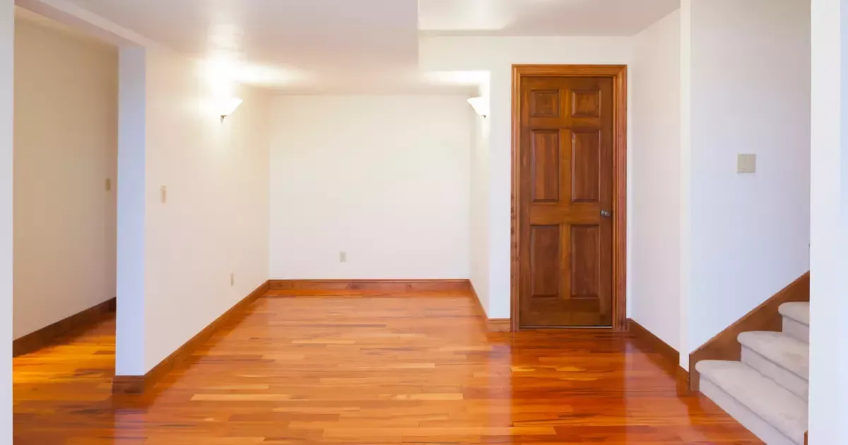An empty basement with hardwood floors and white walls