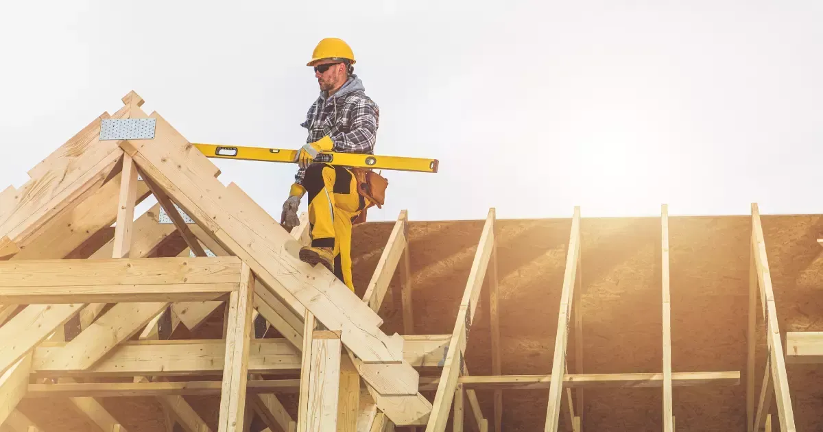 A person in a yellow hard hat and yellow overalls holding a level during house construction