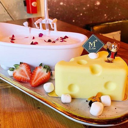 Dessert tray with a yellow cheese-shaped cake, strawberries, and a bowl of pink dessert with decorative toppings.
