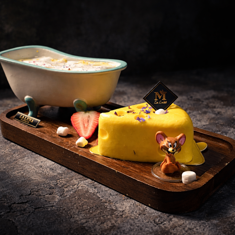 Dessert tray with yellow cake, strawberry, and small mouse figurine beside a bowl of custard on a dark table
