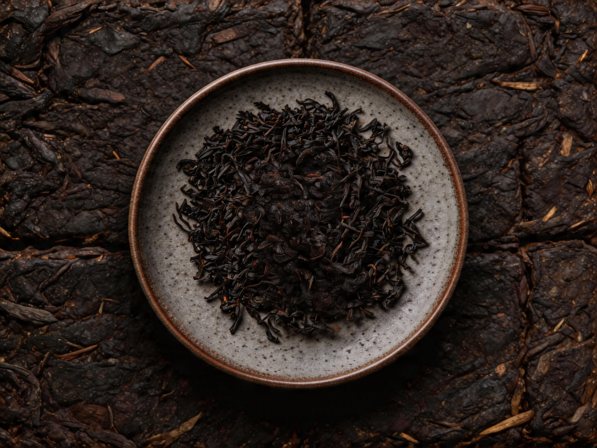 Bowl of loose black tea leaves on a dark textured surface