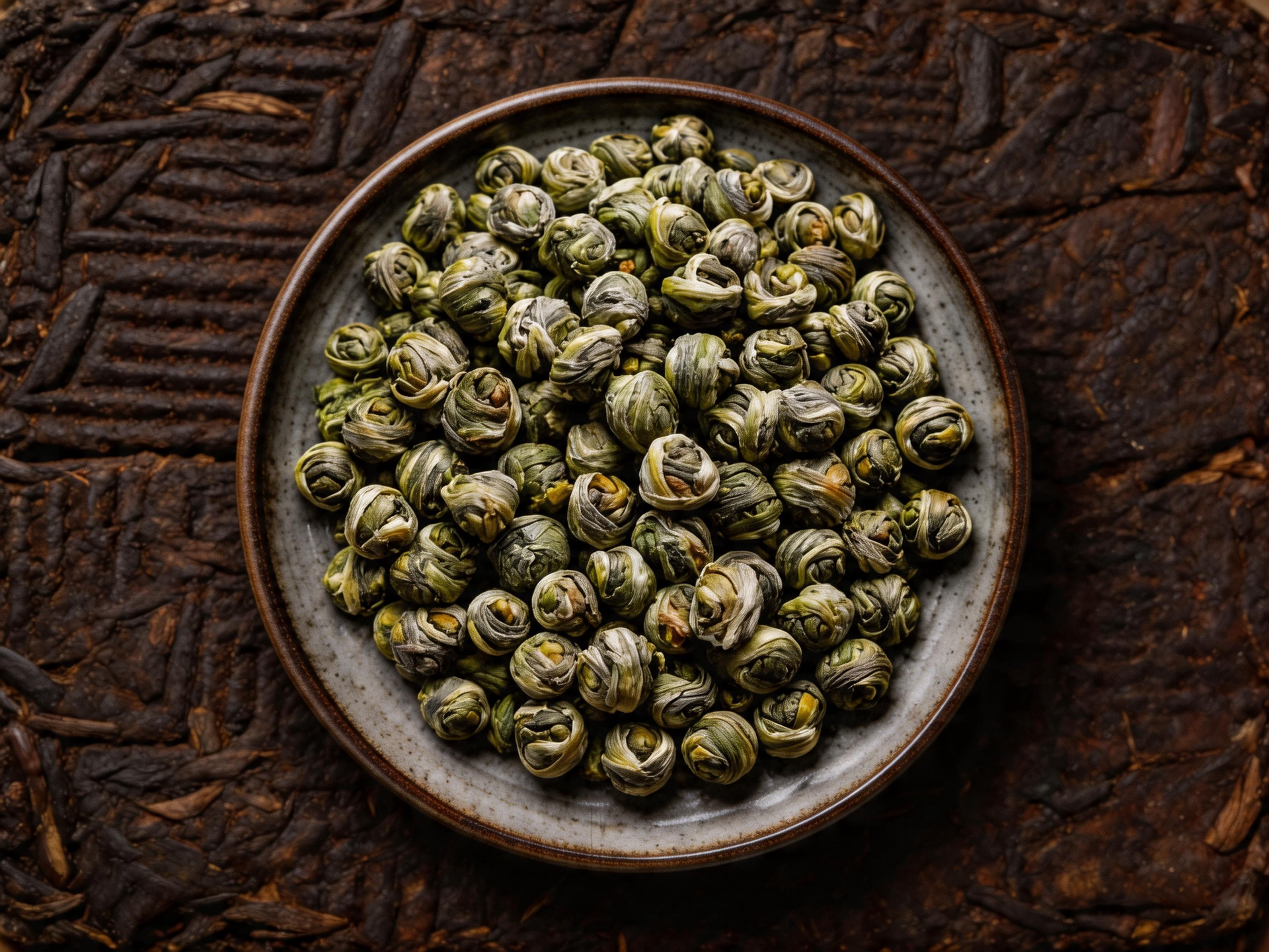 Bowl of dried green tea leaves on a dark rustic wooden surface