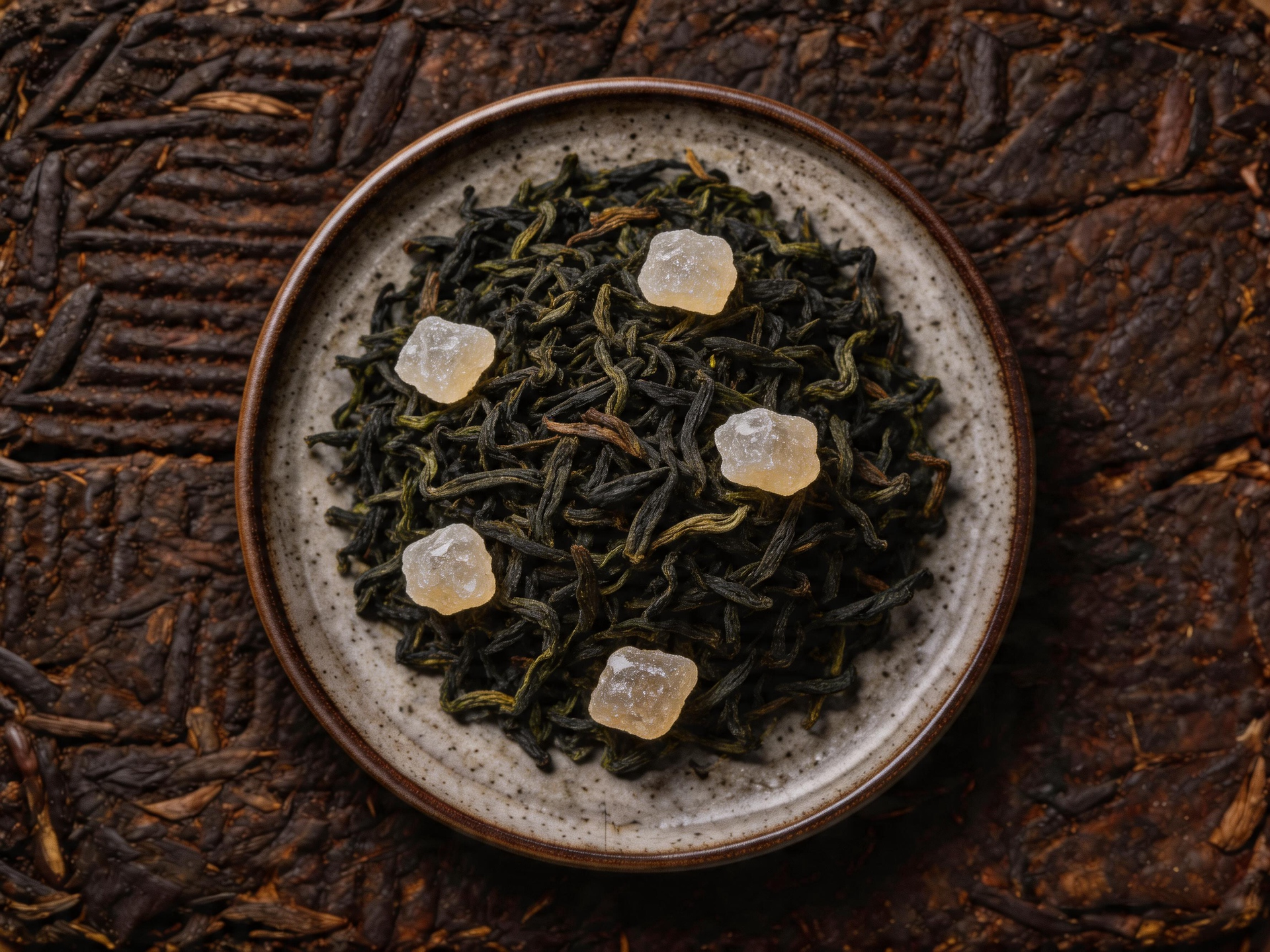 Top-down view of a bowl of loose tea topped with small white sugar cubes on a brown textured surface