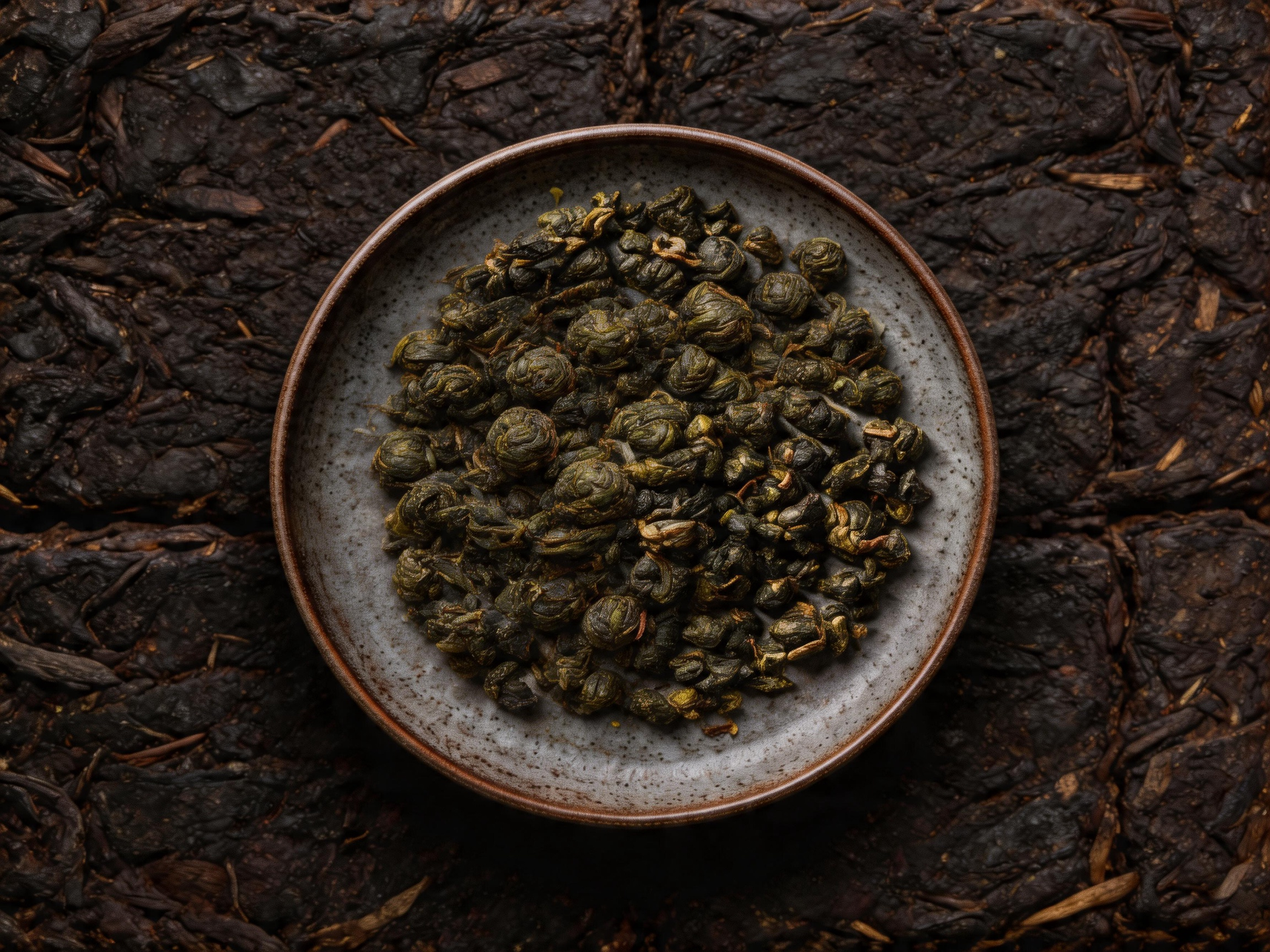 A bowl of dried green tea leaves on a dark, textured surface.