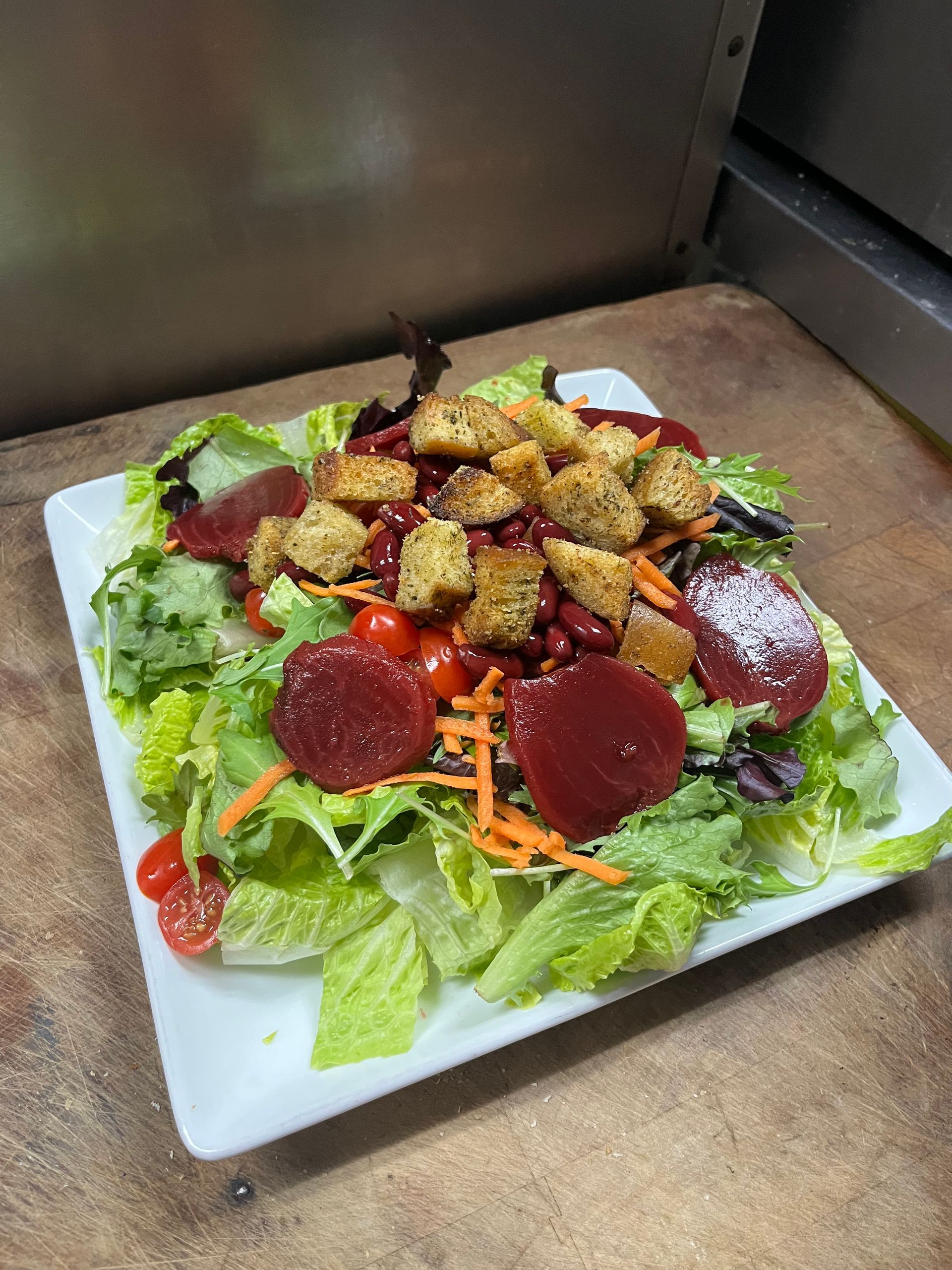 Salad with lettuce, beets, croutons, and tomatoes on a white square plate.