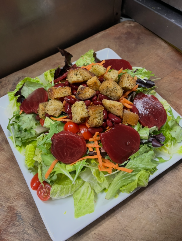 Salad with lettuce, beets, croutons, carrots, and tomatoes on a white plate.