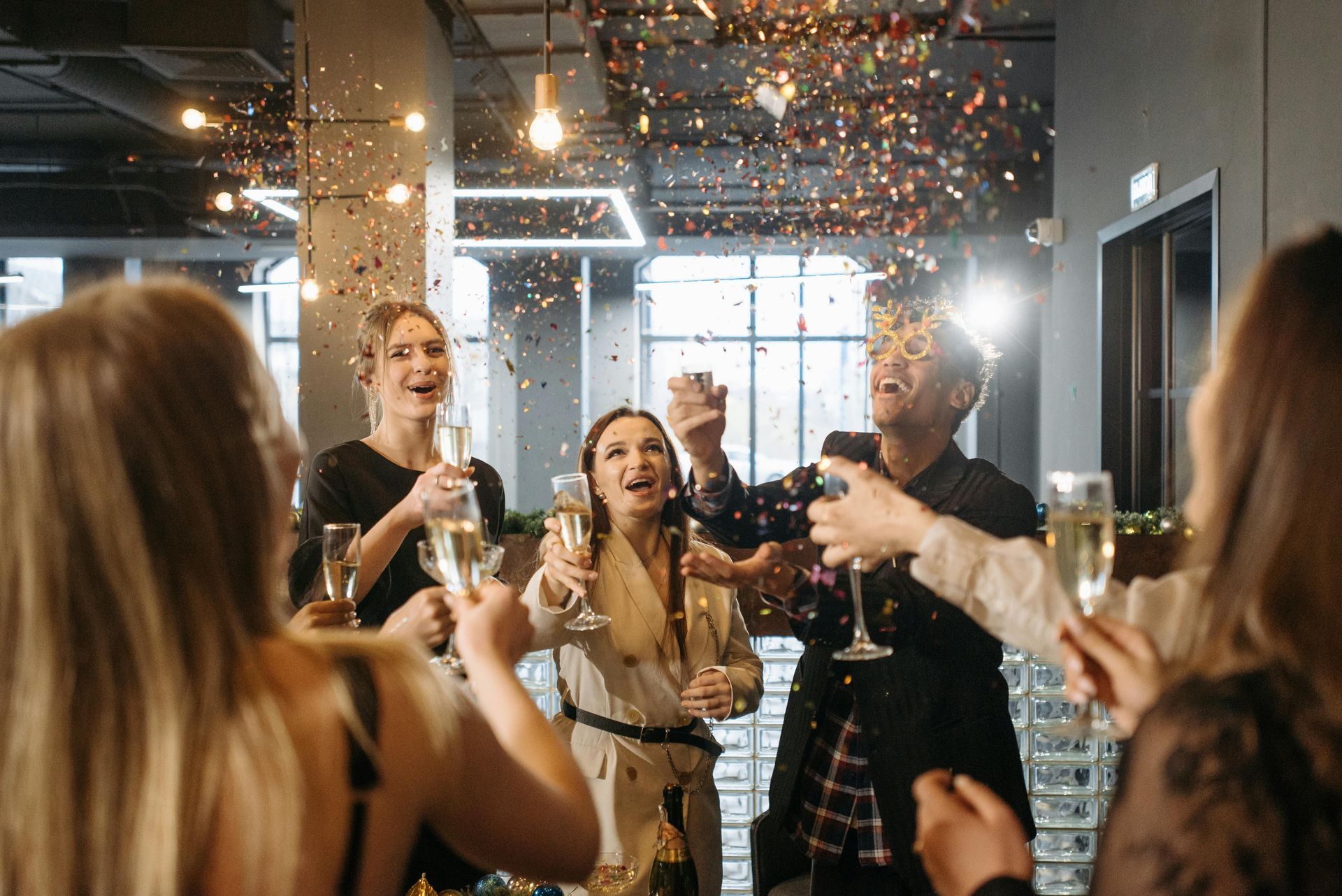 People are celebrating, throwing confetti, and holding champagne glasses in a festive indoor setting