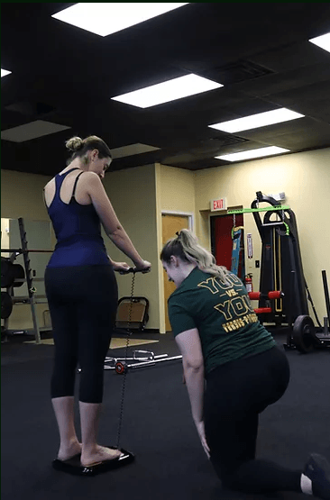 A professional assisting a person standing on a body composition scale in a gym.