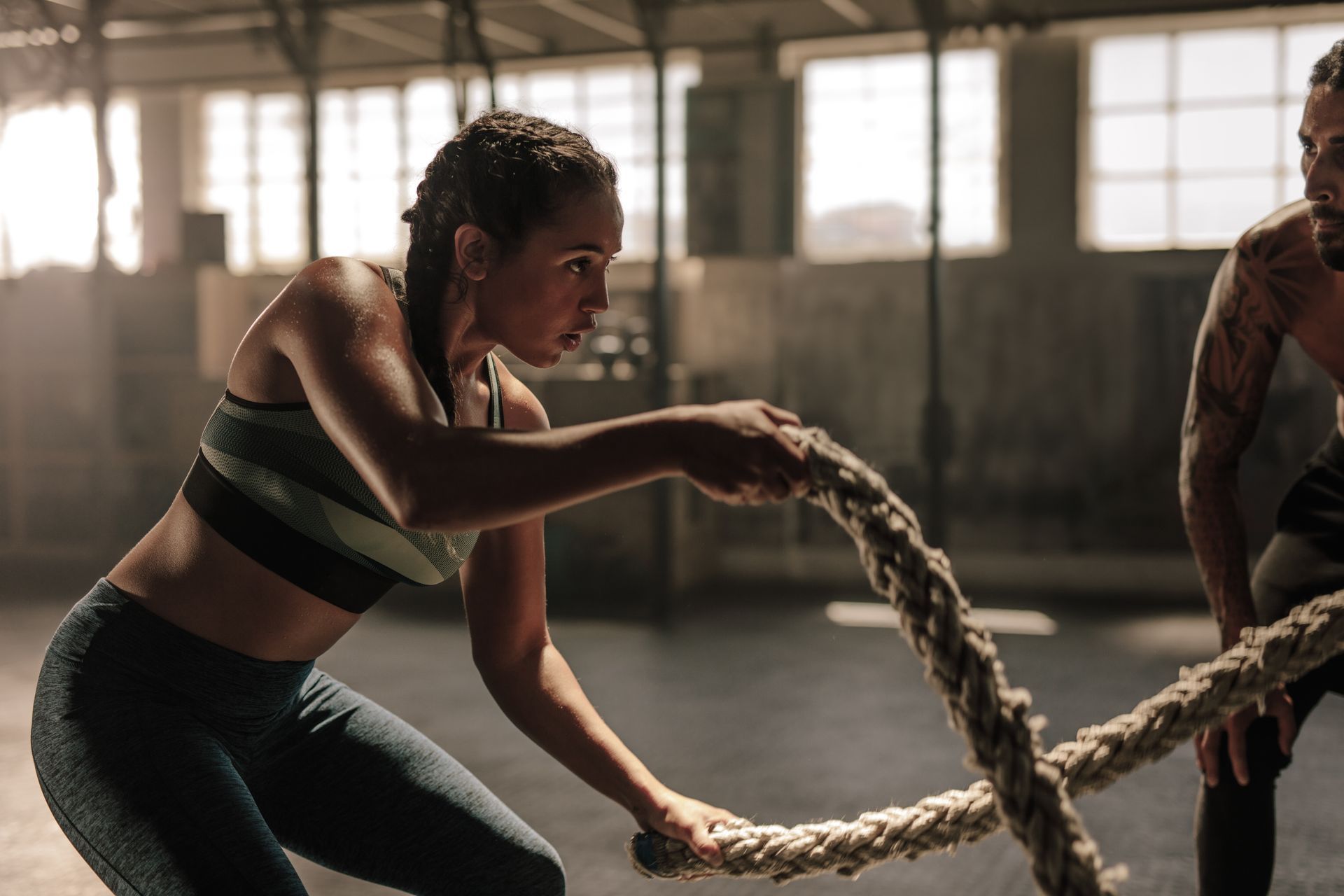 A person performs a battle rope exercise in a gym while a partner observes from the side.