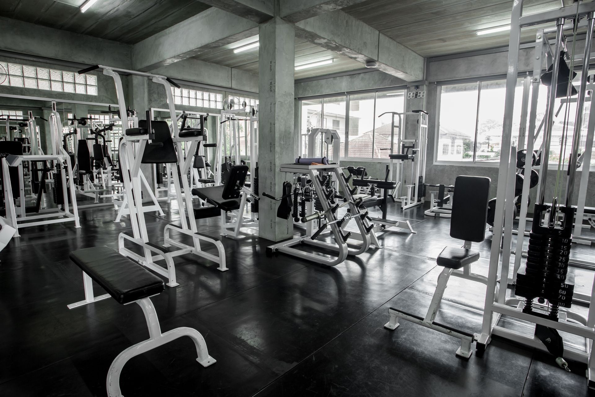 A monochromatic, wide-angle view of a fitness gym filled with various weightlifting equipment and exercise machines.