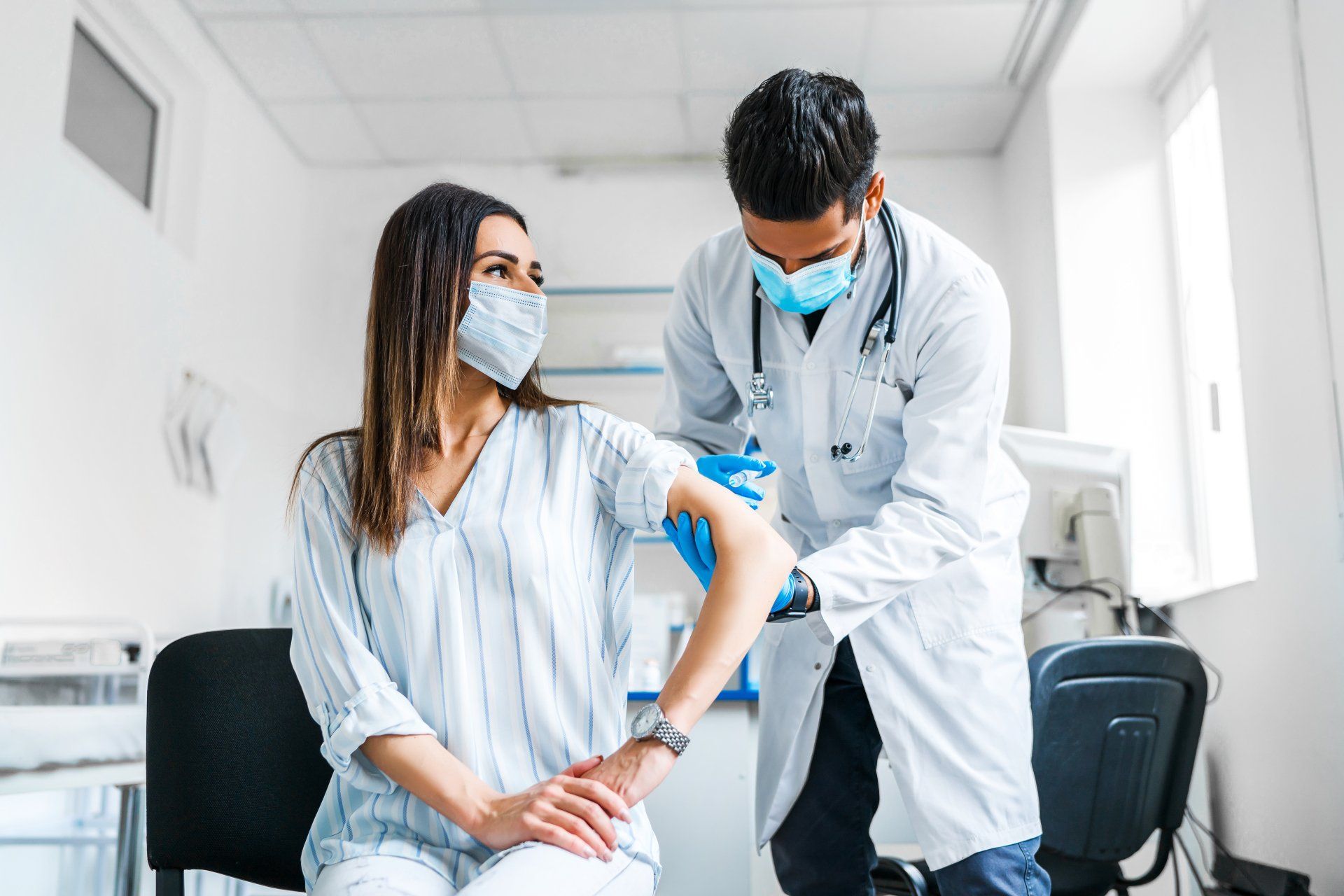 A doctor is giving a vaccine to a patient who is wearing a mask.