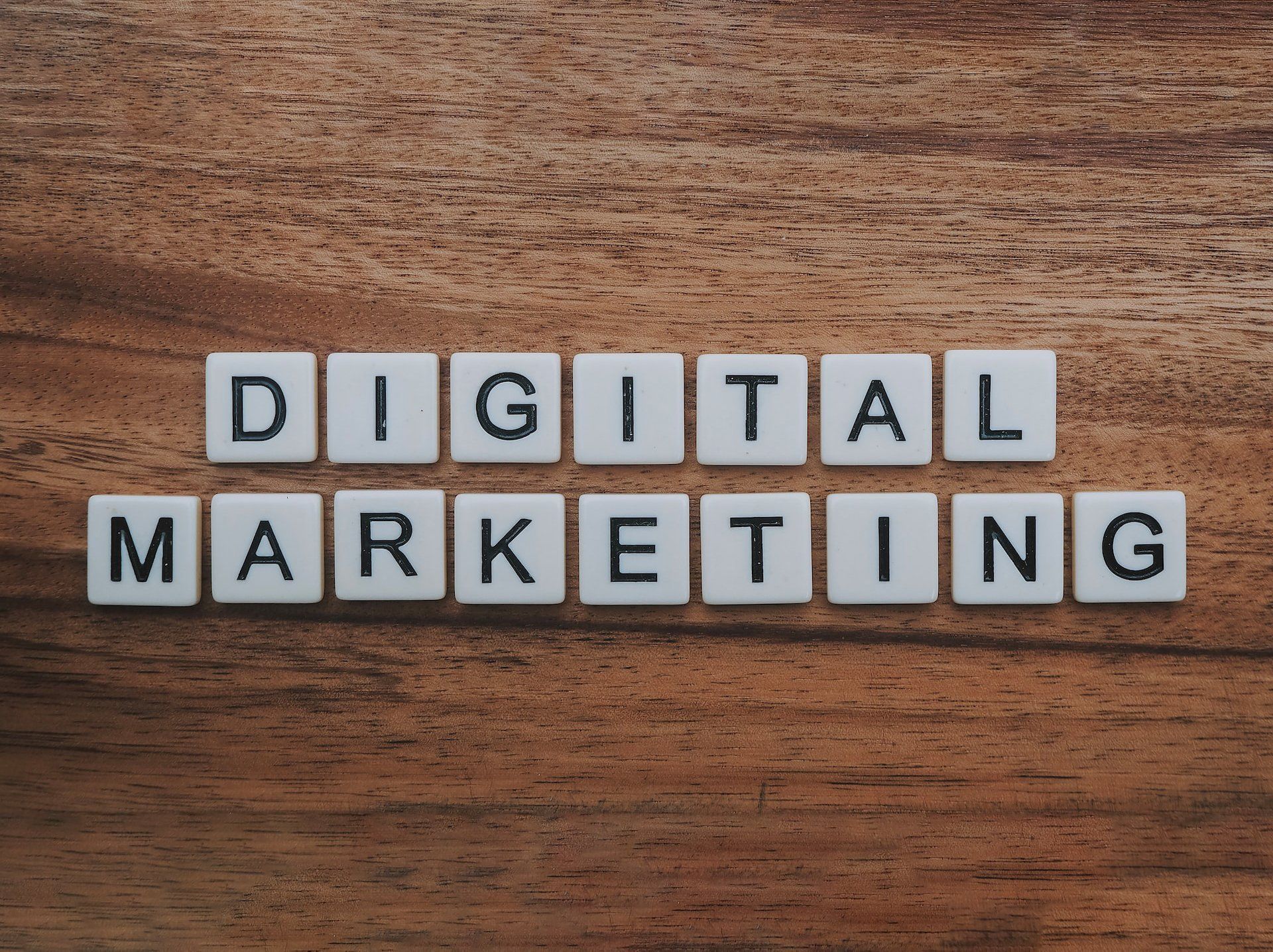 The word digital marketing is written in white tiles on a wooden table.