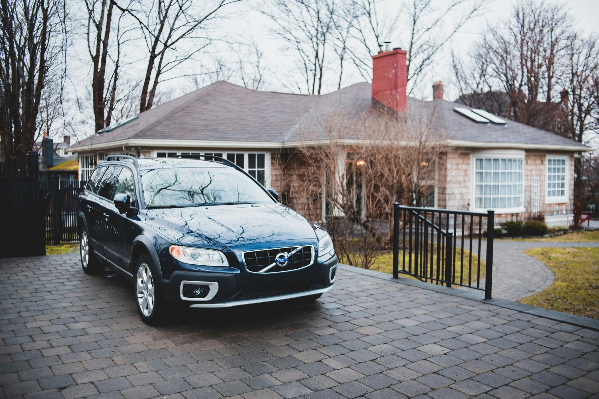 Black Volvo SUV parked in a driveway beside a brick house on a cloudy day