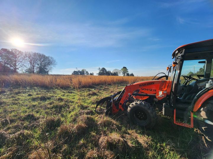 Orange tractor working in a grassy field at sunset
