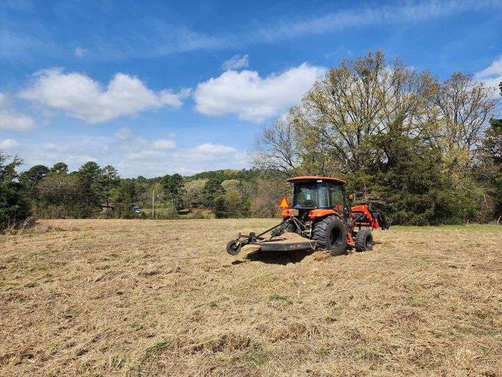 Orange tractor tilling a dry field under a blue sky with clouds