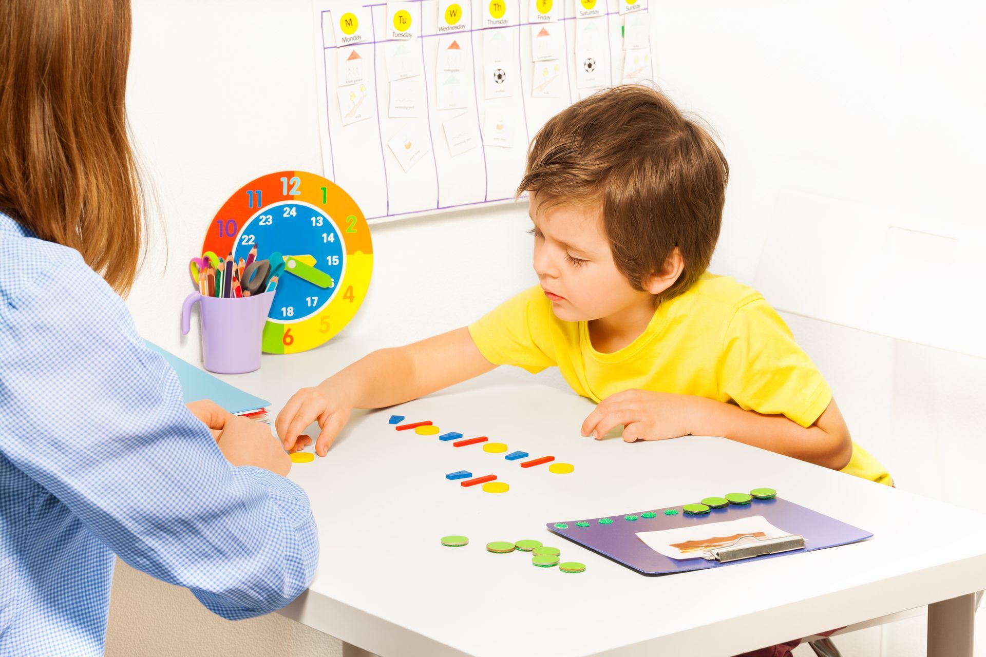 A young boy is sitting at a table playing with a woman.