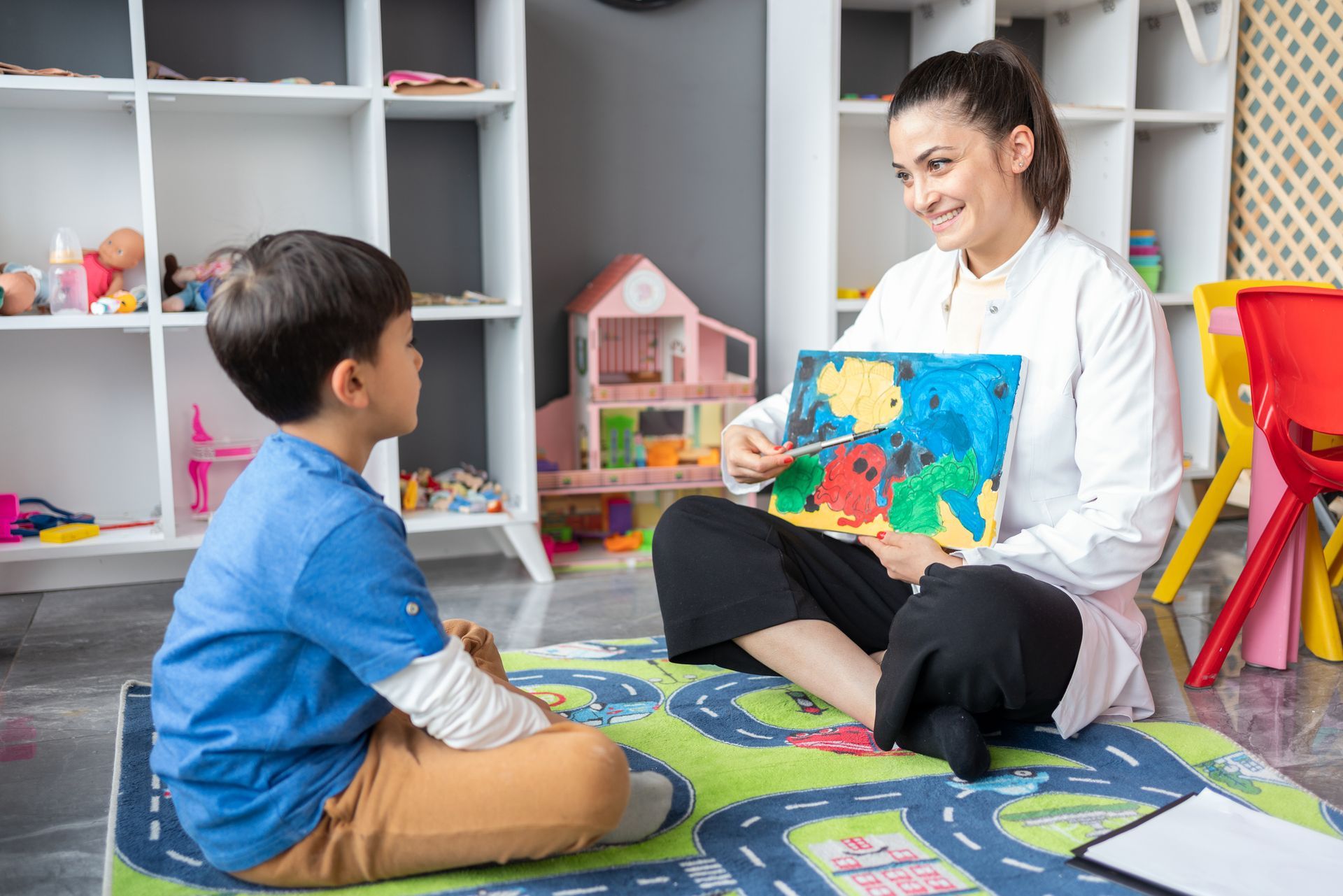 A woman is sitting on the floor reading a book to a young boy.