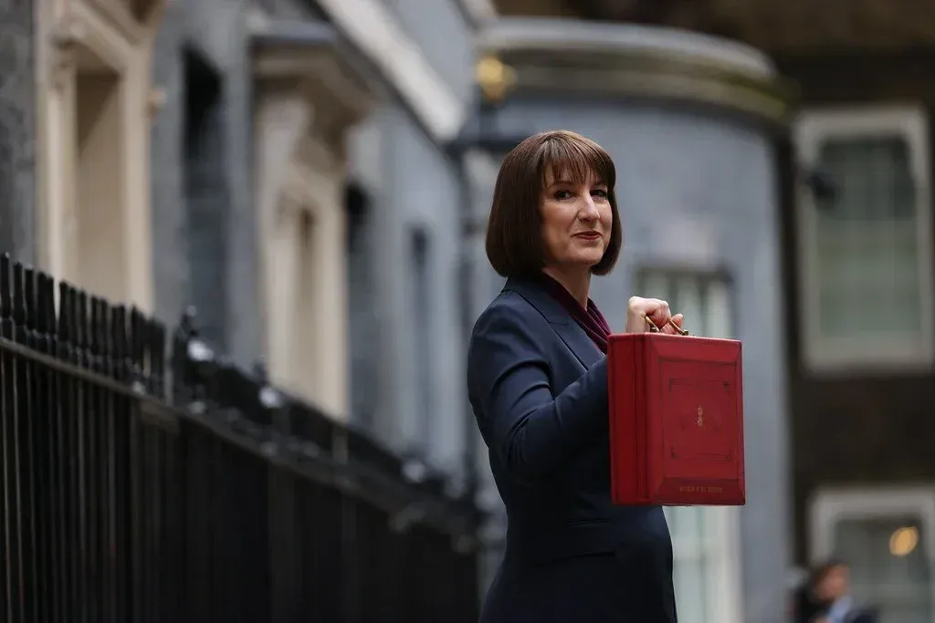 Woman in a suit, holding a red briefcase, stands outside a building with a dark façade.