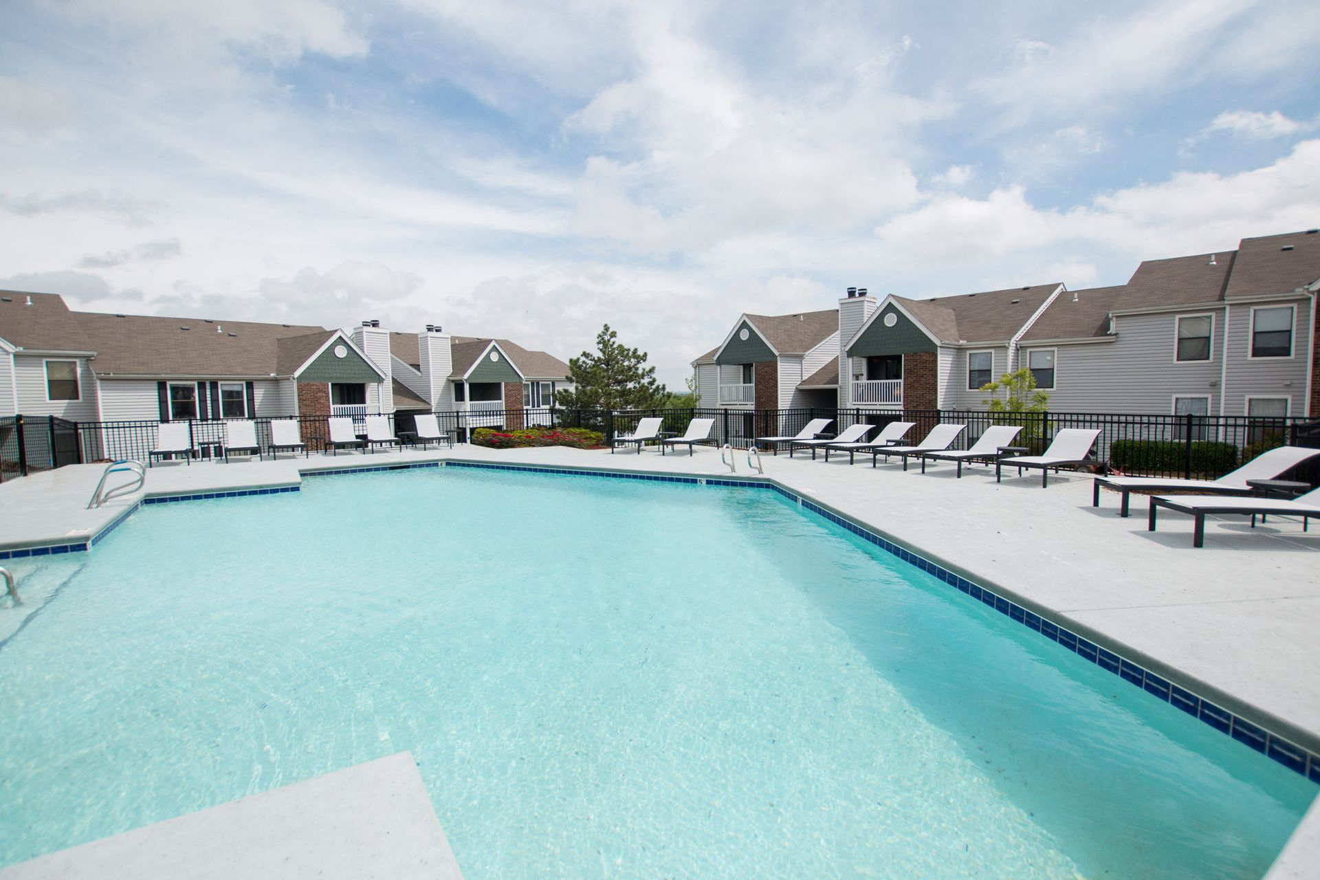 A large swimming pool surrounded by chairs in front of a row of houses.