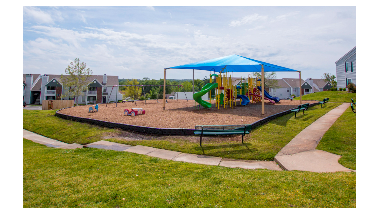 There is a playground with a blue umbrella over it.