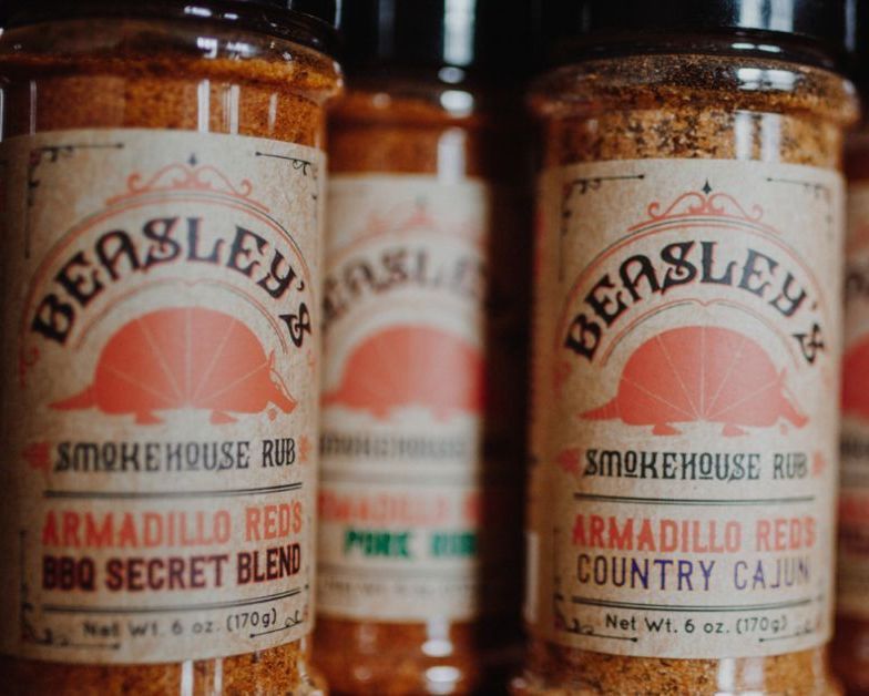 Three bottles of beasley 's smokehouse rub are lined up on a table.