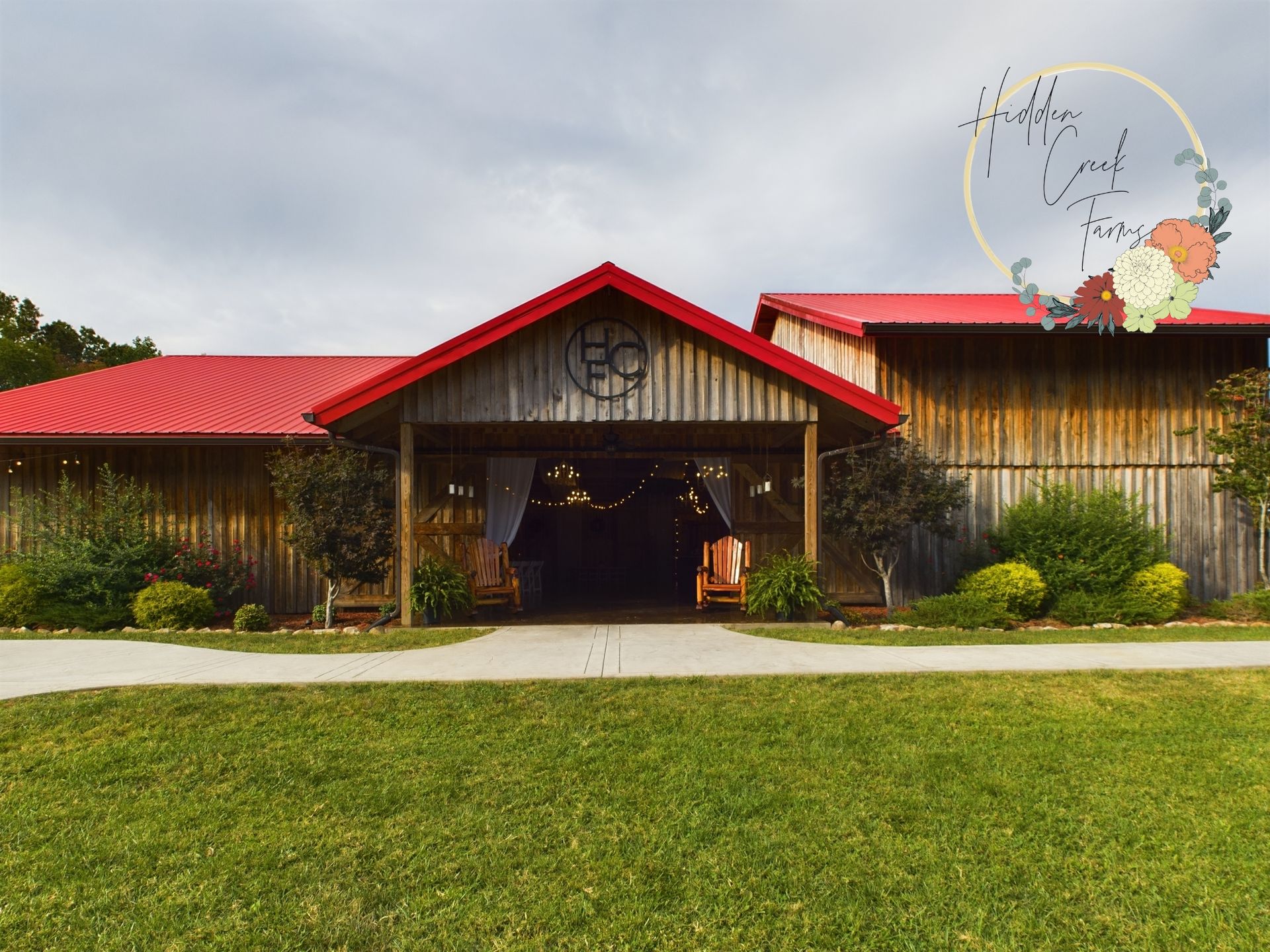 A large barn with a red roof is surrounded by grass and trees.