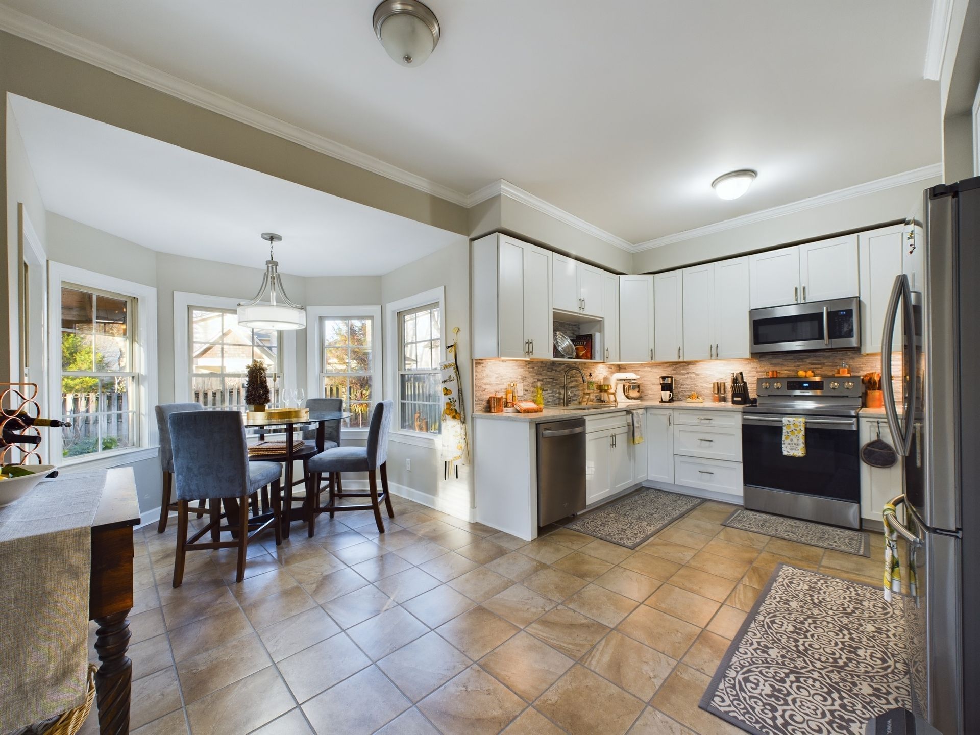 A kitchen with white cabinets and stainless steel appliances and a dining room with a table and chairs.