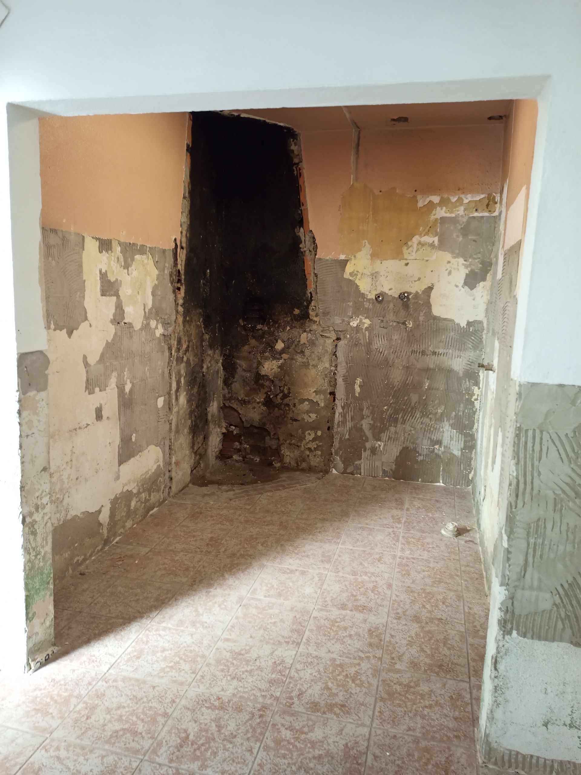 Quarto interior com paredes danificadas; gesso e tinta expostos; área escura e recuada.