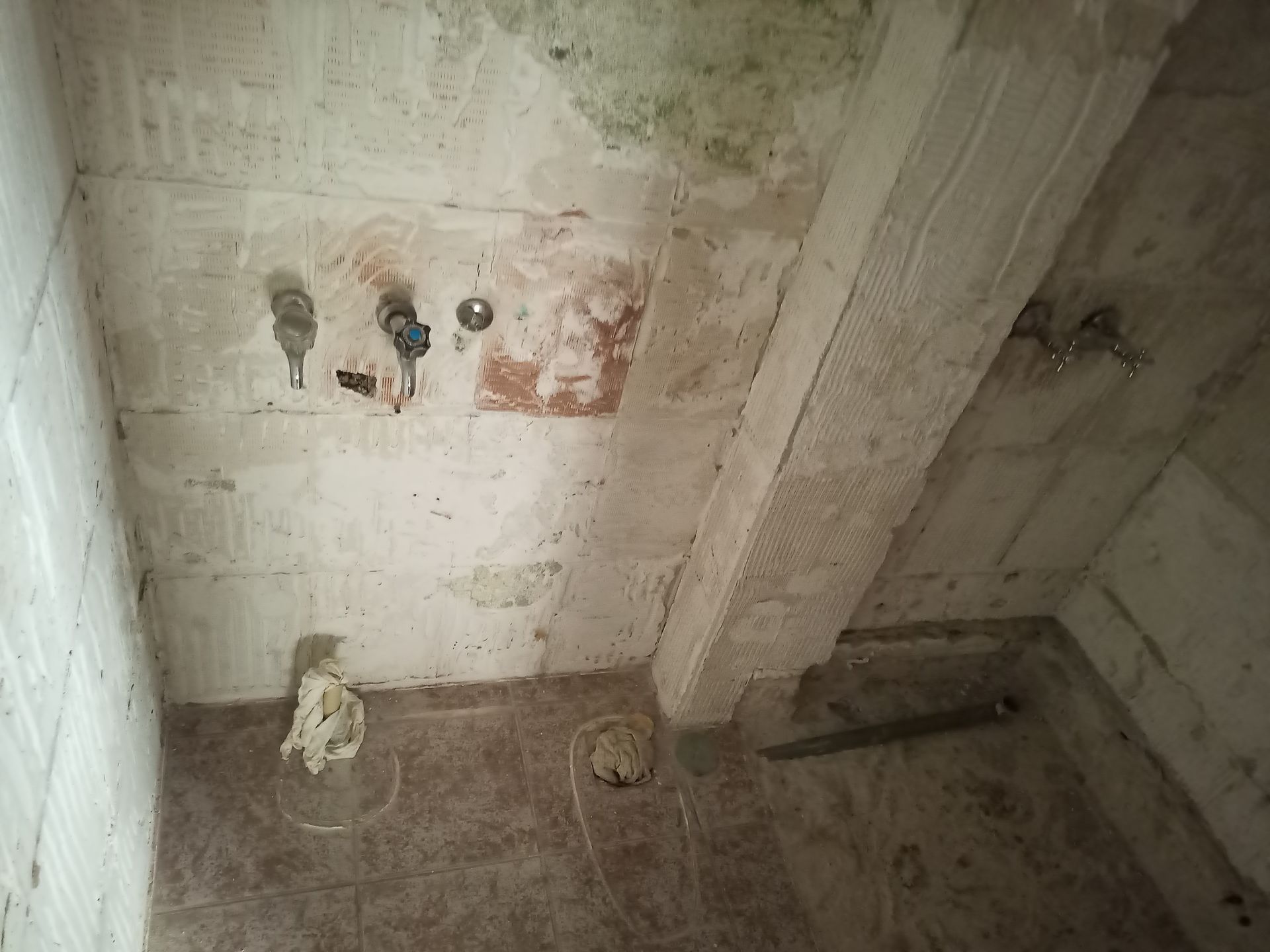 Box de chuveiro em concreto aparente com encanamento e azulejos expostos.