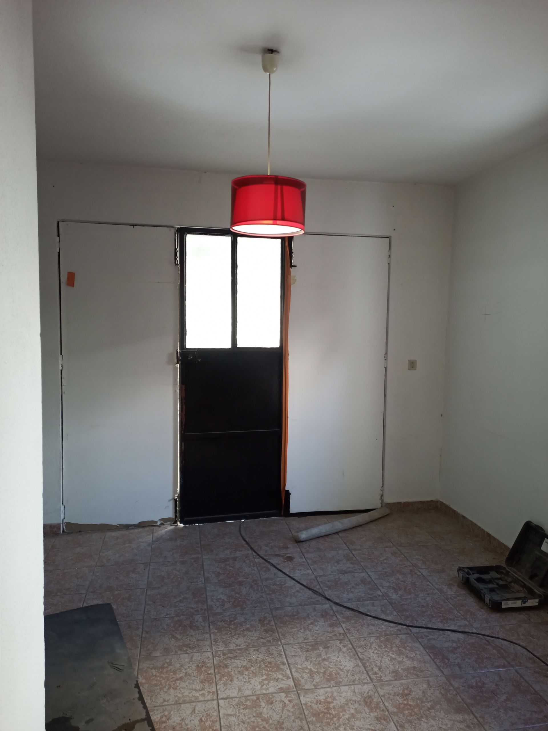 Quarto interior com porta escura, abajur vermelho e parede de gesso. Piso revestido com azulejos.