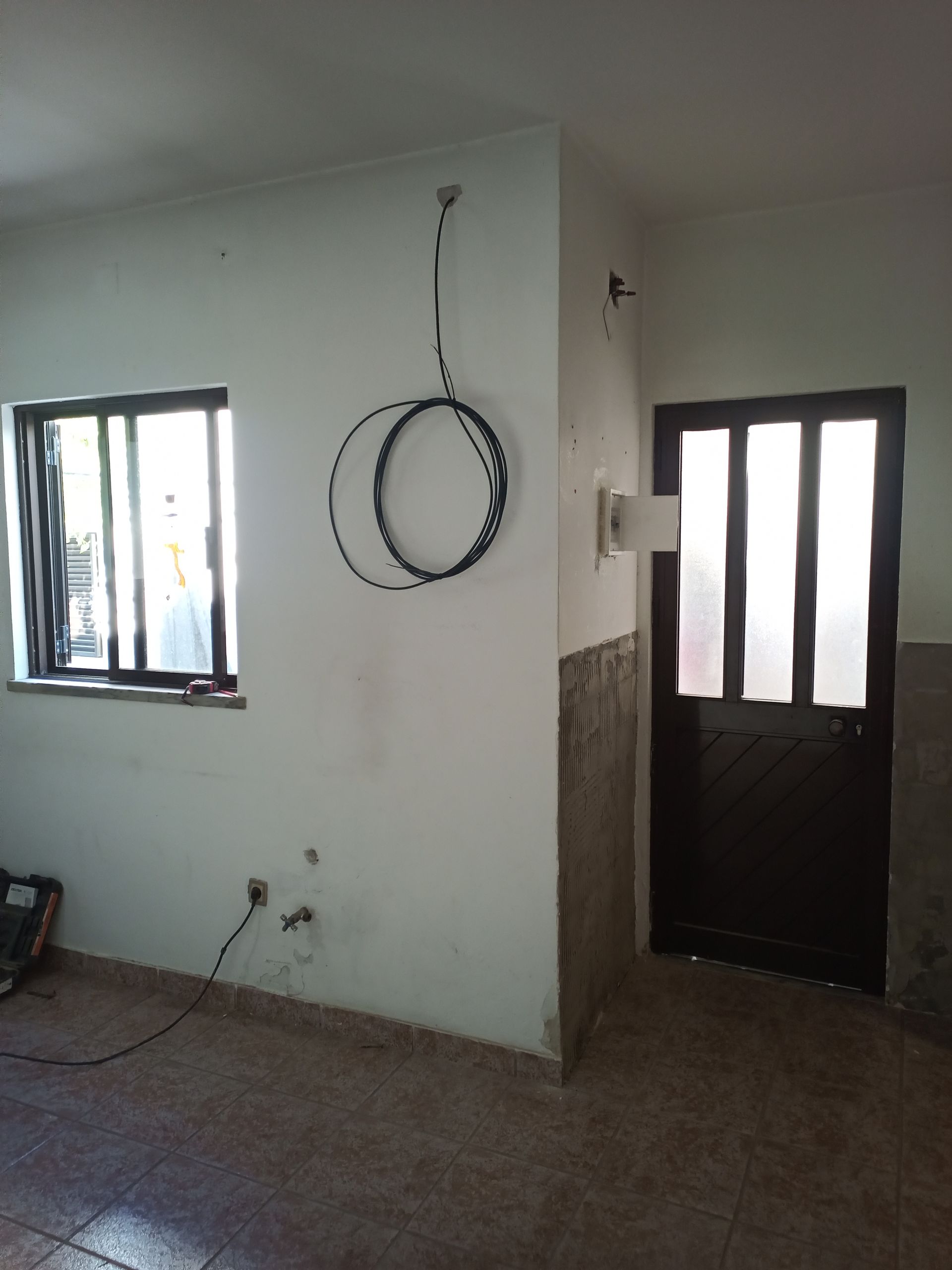 Quarto interior com janela, porta e cabo preto enrolado pendurado na parede.