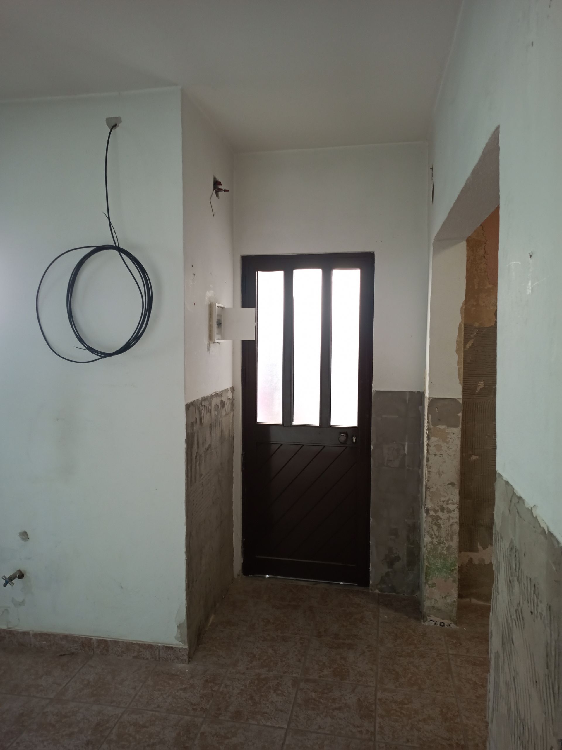 Corredor com porta escura, paredes parcialmente inacabadas e cabo preto enrolado.