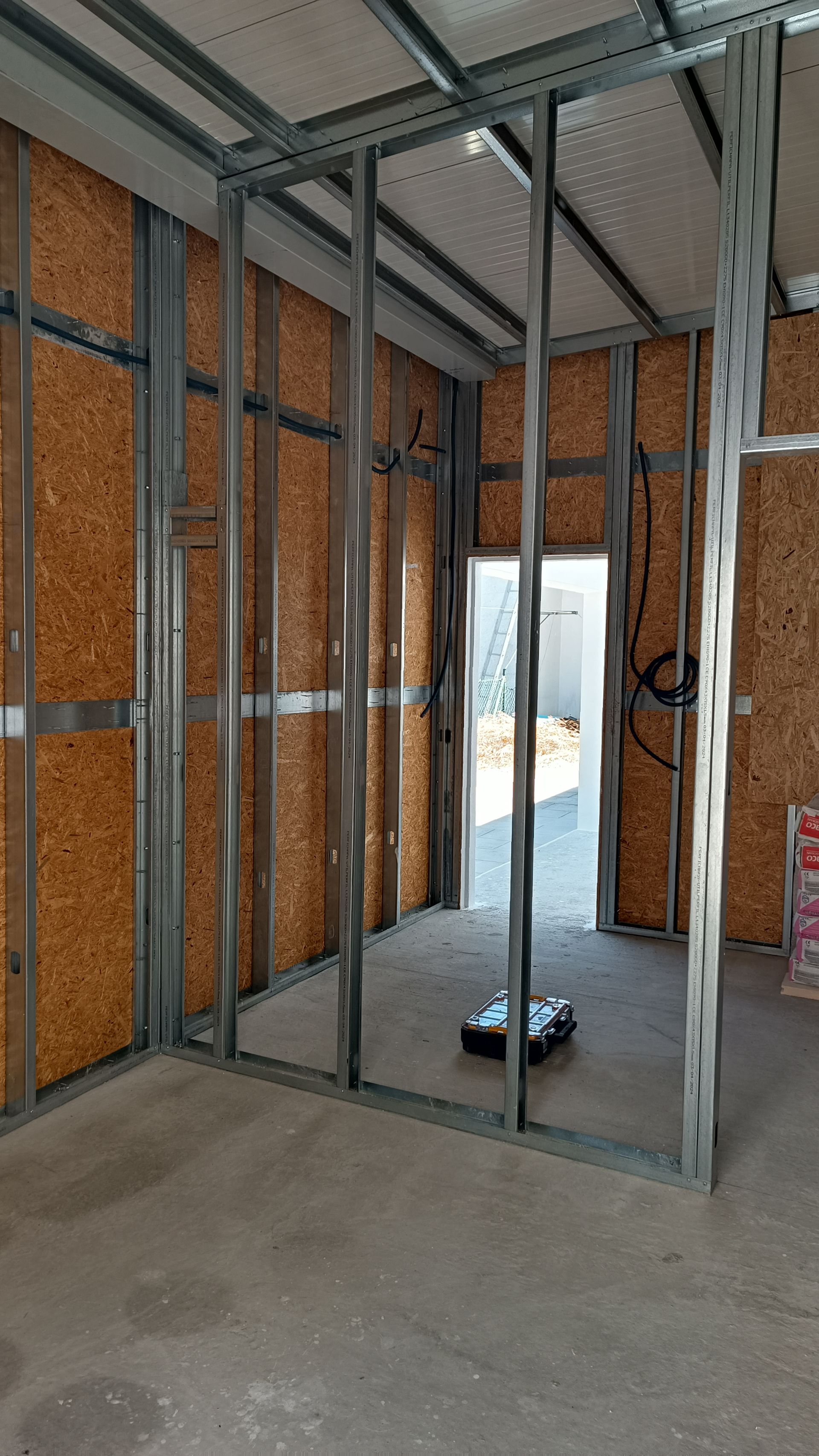 Interior de um cômodo em construção; estrutura de metal sobre paredes de OSB (painel de madeira orientada); porta visível.