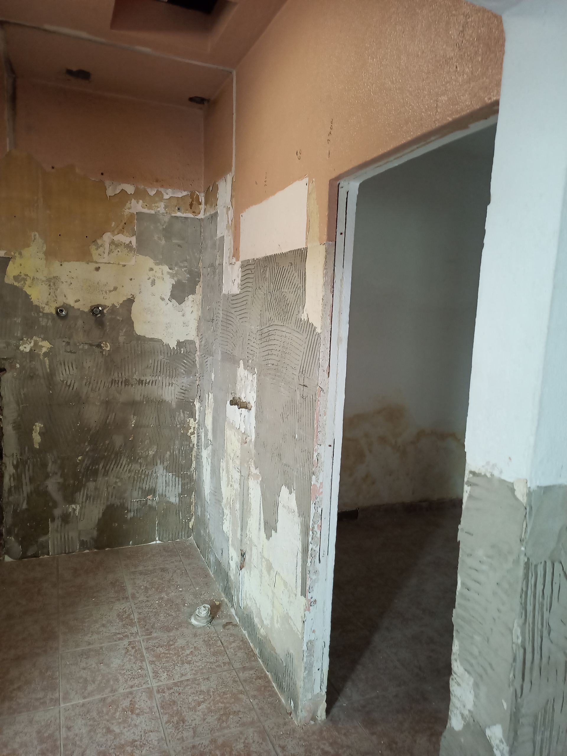 Quarto interior em construção, com paredes expostas, porta e piso de azulejo.