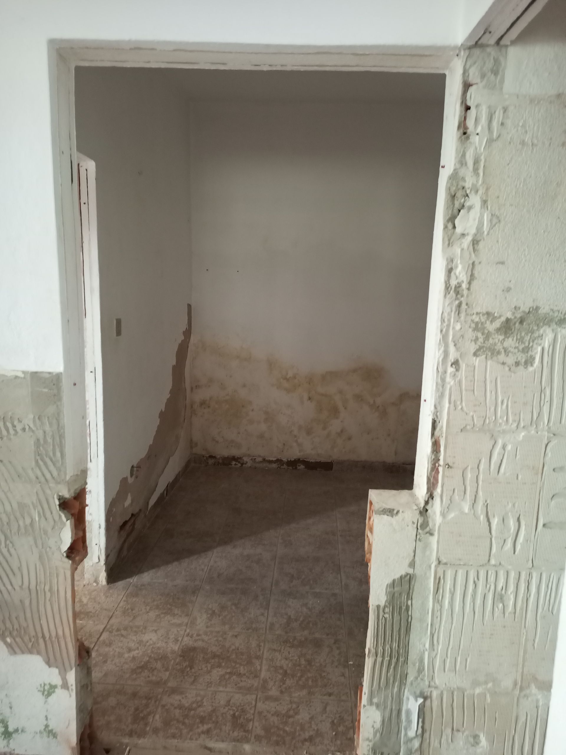 Um pequeno cômodo inacabado com danos causados ​​pela água na parte inferior das paredes e na porta.