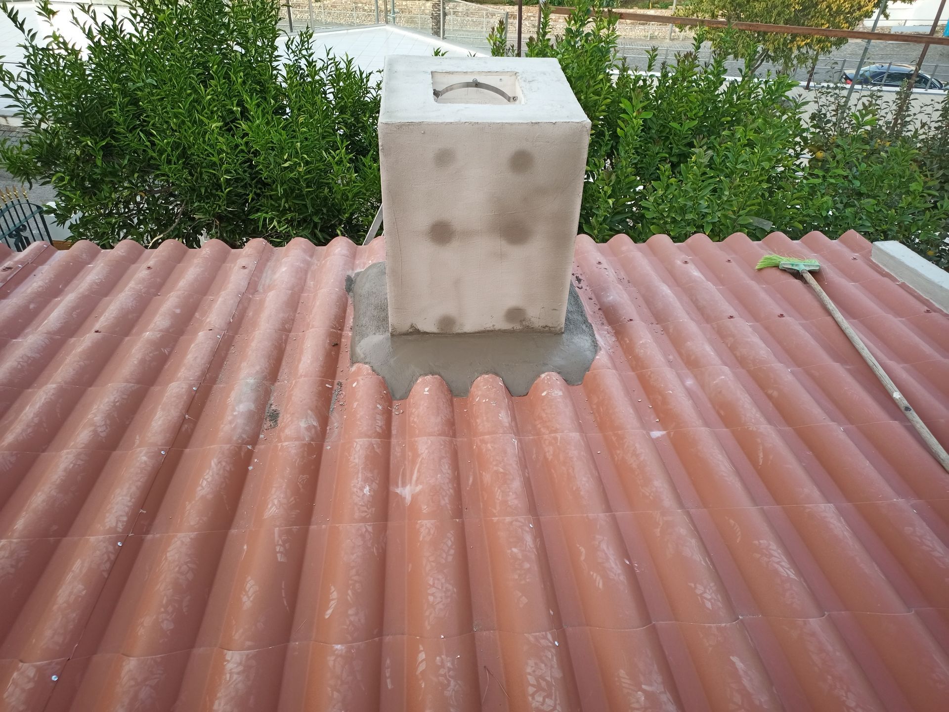 Chaminé de concreto sobre um telhado ondulado avermelhado, em contraste com a folhagem verde.