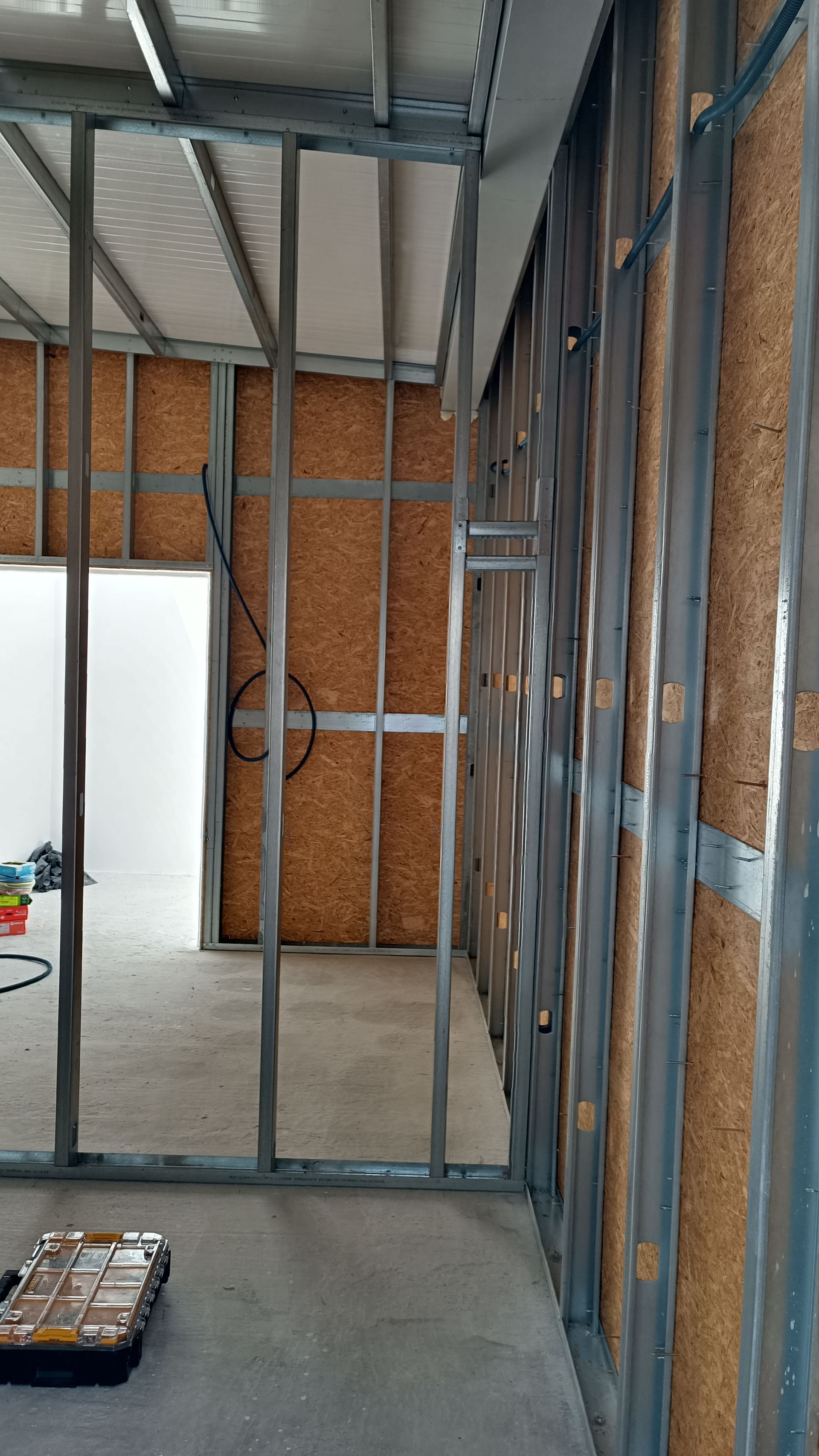 Estrutura metálica de um cômodo em construção. O revestimento de OSB é visível, assim como a porta aberta.