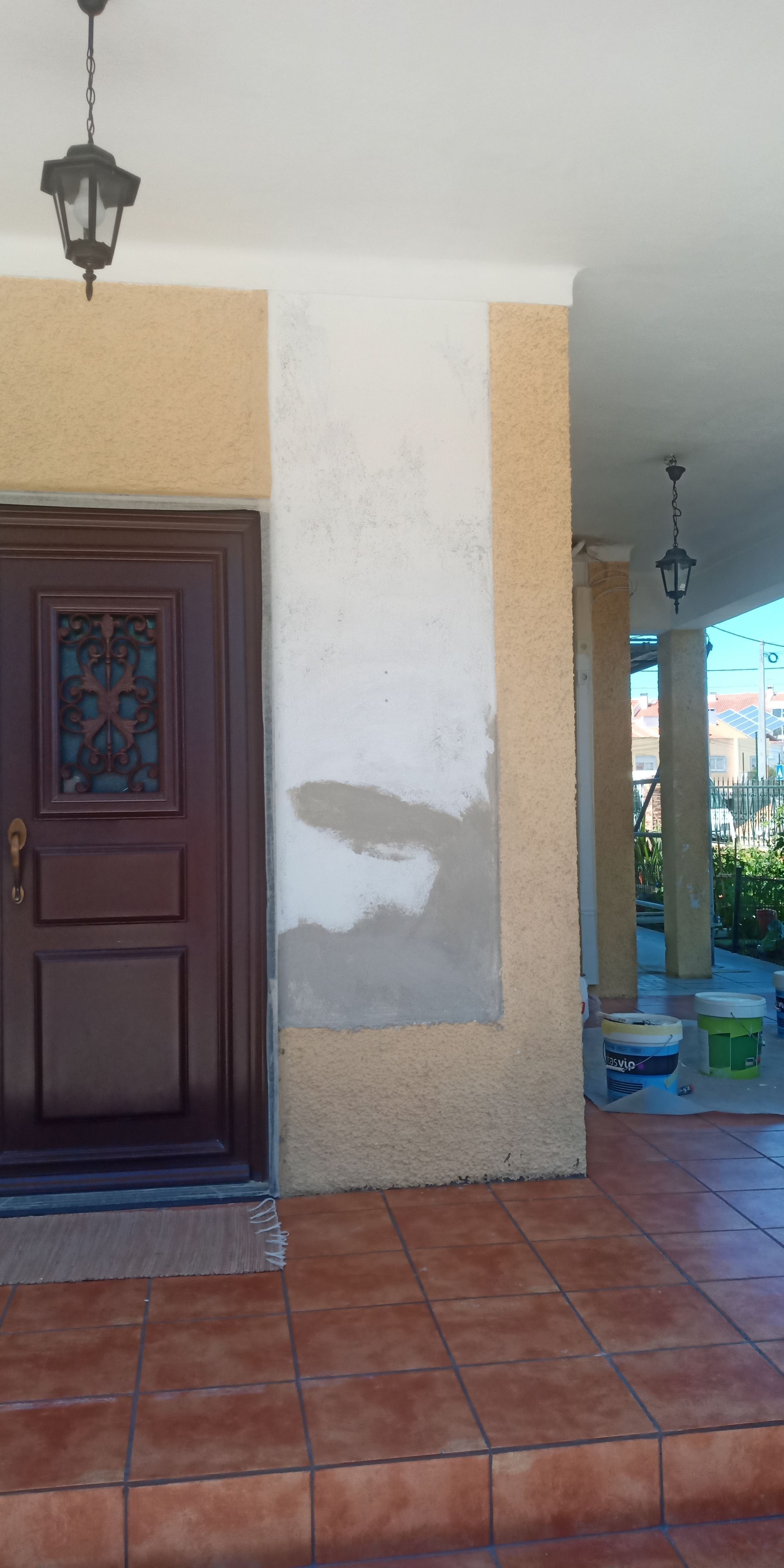 Hall de entrada com porta marrom escura, paredes em tons creme e amarelo e piso de ladrilho de terracota.