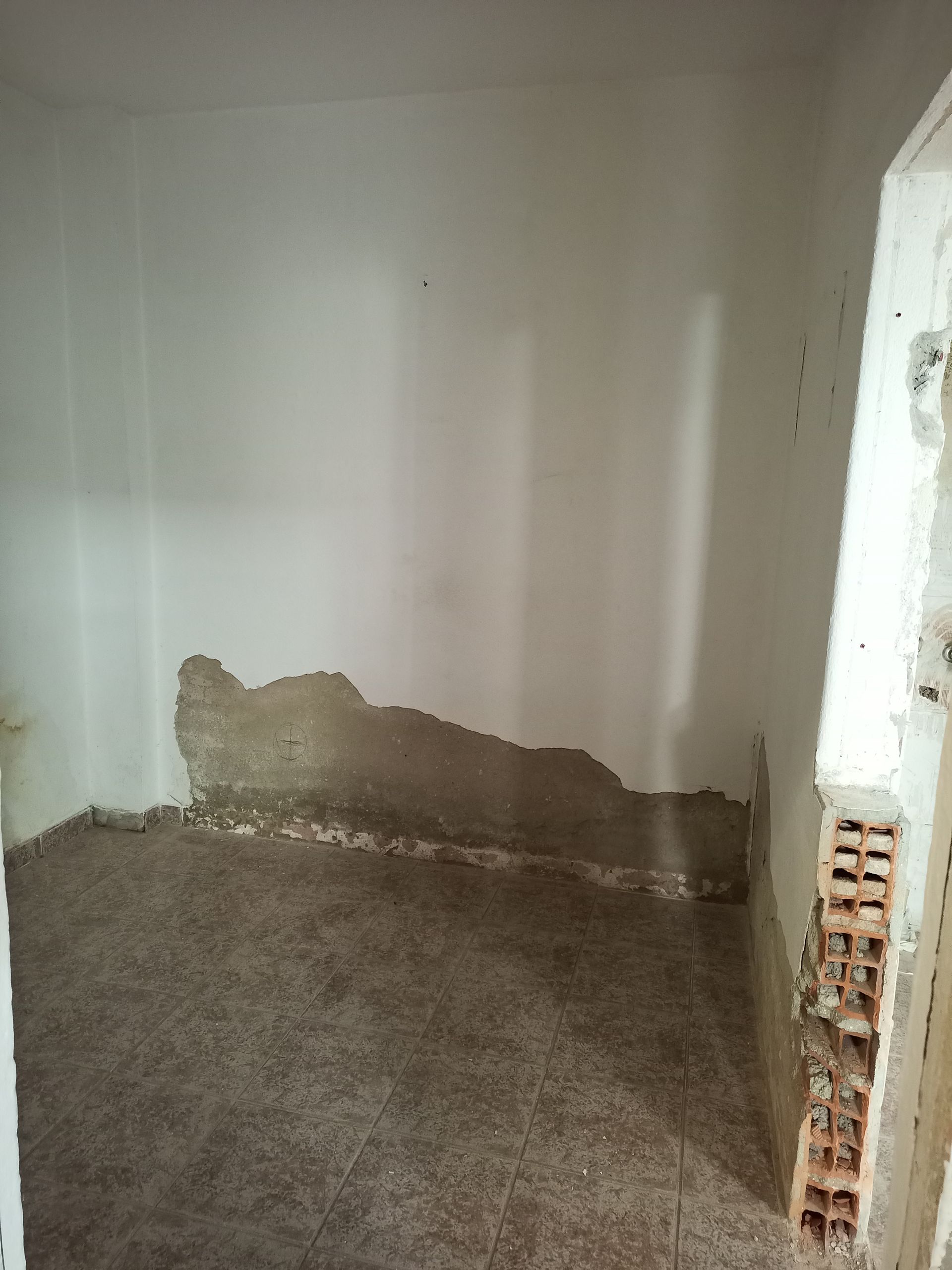 Danos causados ​​pela água em um cômodo pequeno. Tinta descascando e reboco esfarelando perto do chão, expondo a parede de tijolos.