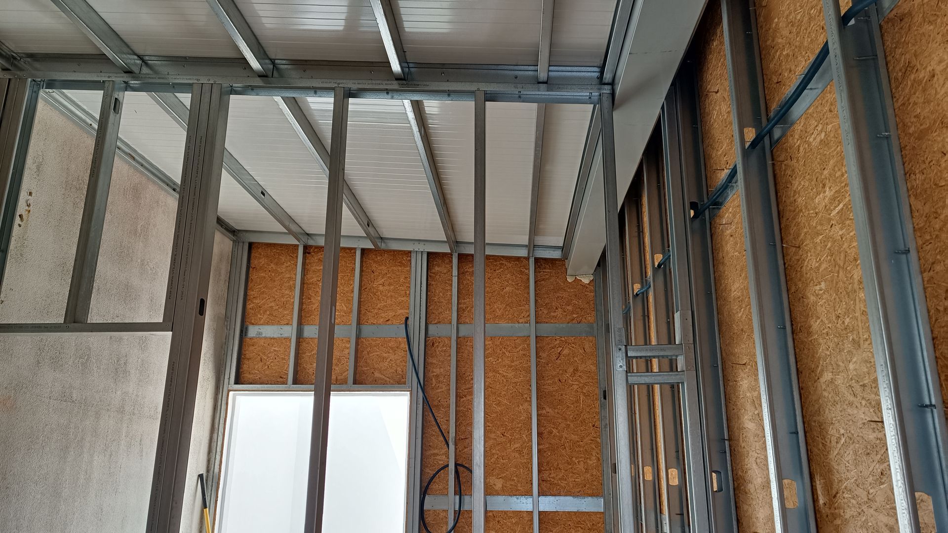 Estrutura metálica de um cômodo em construção com vigas de teto e montantes de parede expostos.