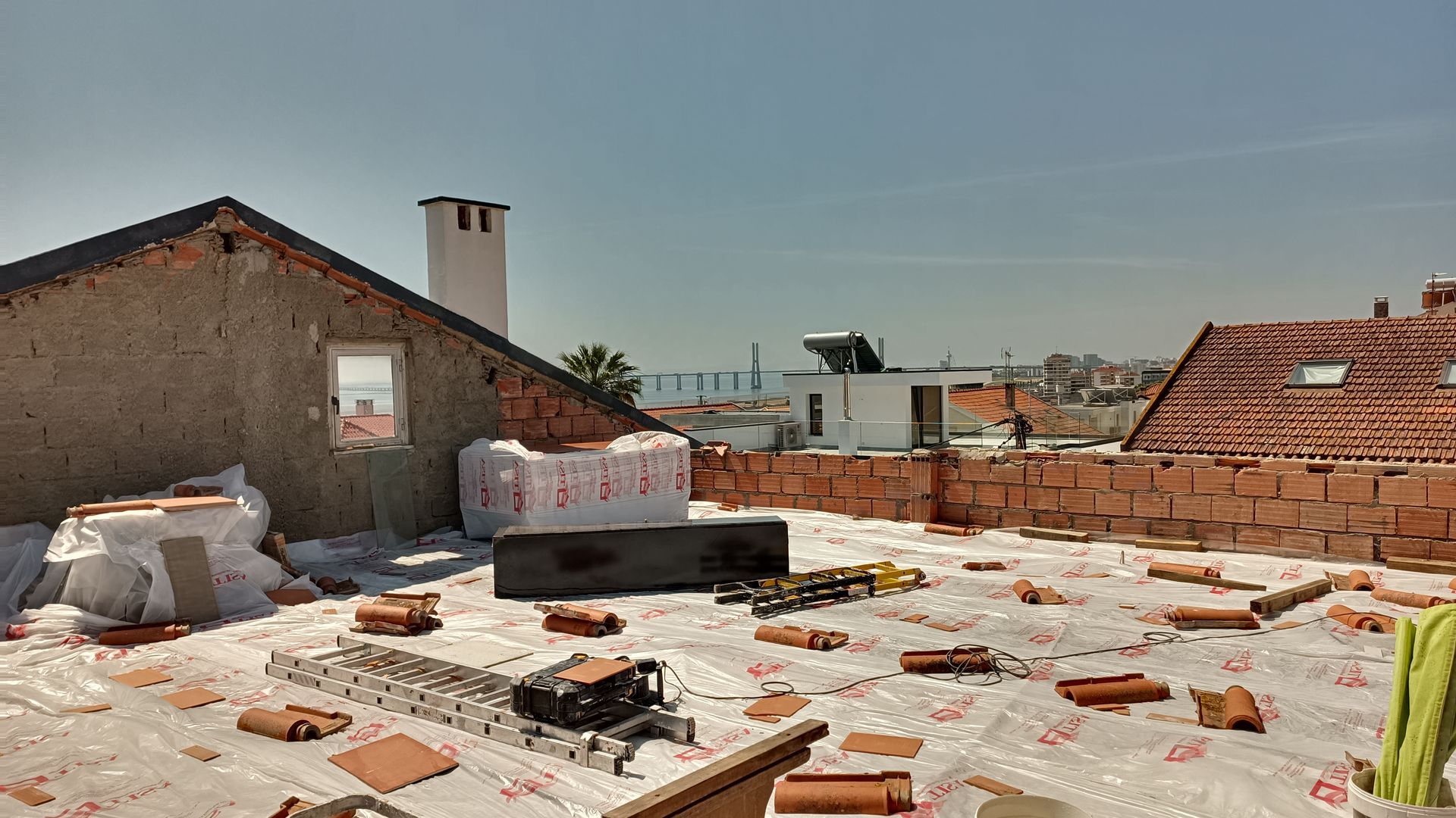 Construção no telhado: Telhas vermelhas, isolamento, ferramentas e materiais estão dispostos. Em um dia ensolarado, as estruturas e uma chaminé são visíveis.