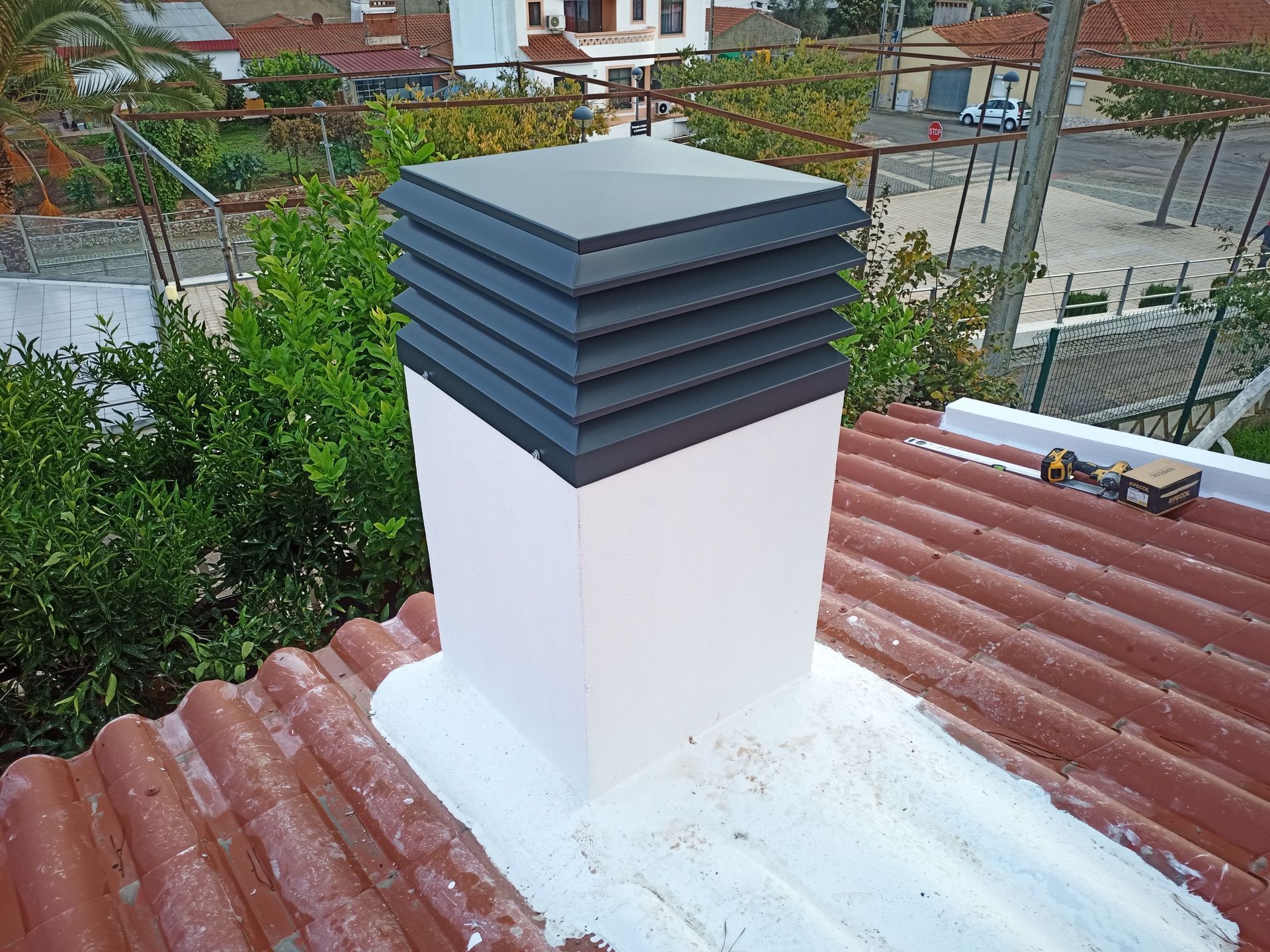 Chaminé em um telhado vermelho de zinco ondulado, encimada por uma cobertura escura em camadas.