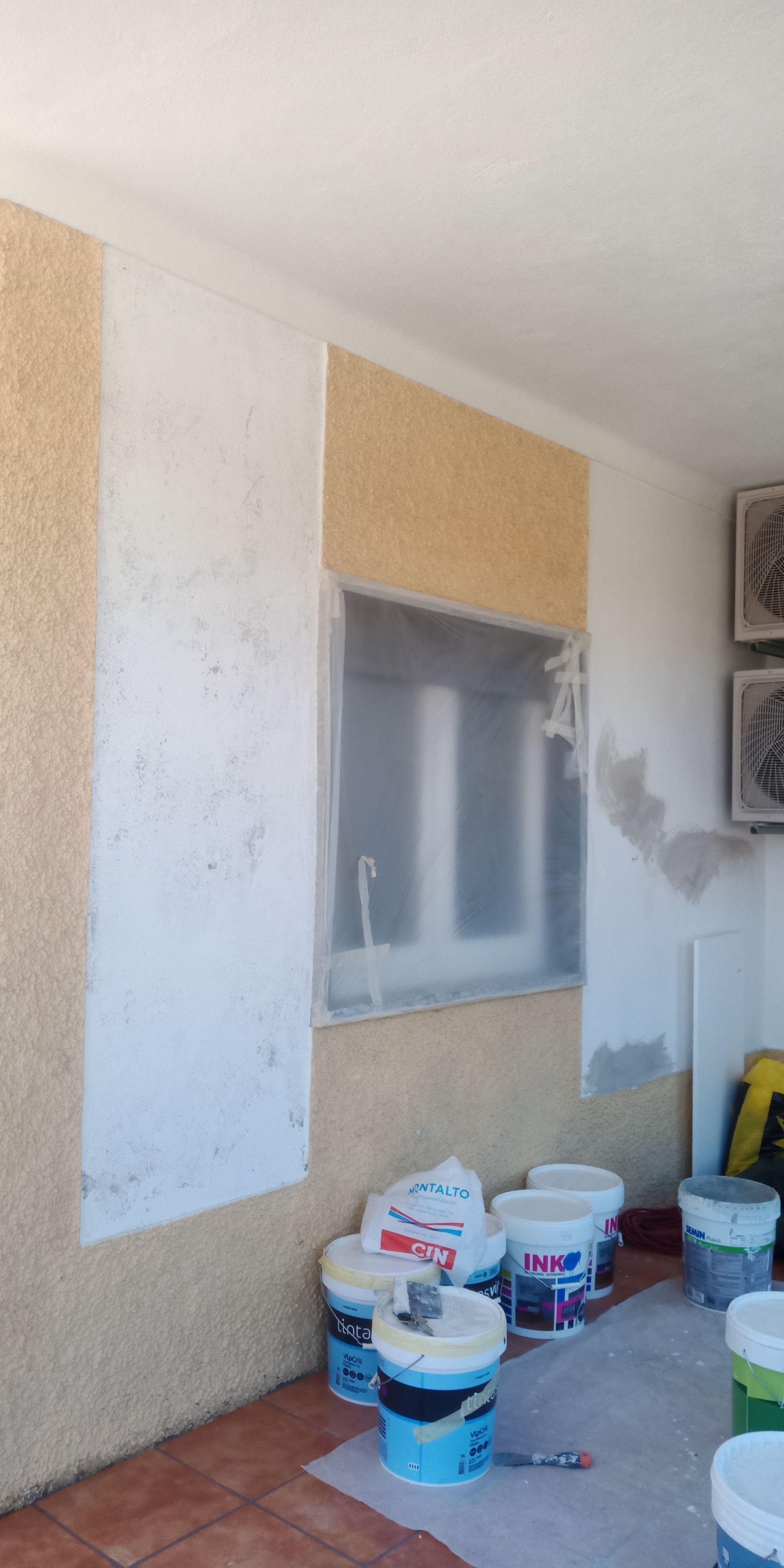 Um quarto em reforma, com baldes de tinta e uma janela coberta com plástico.