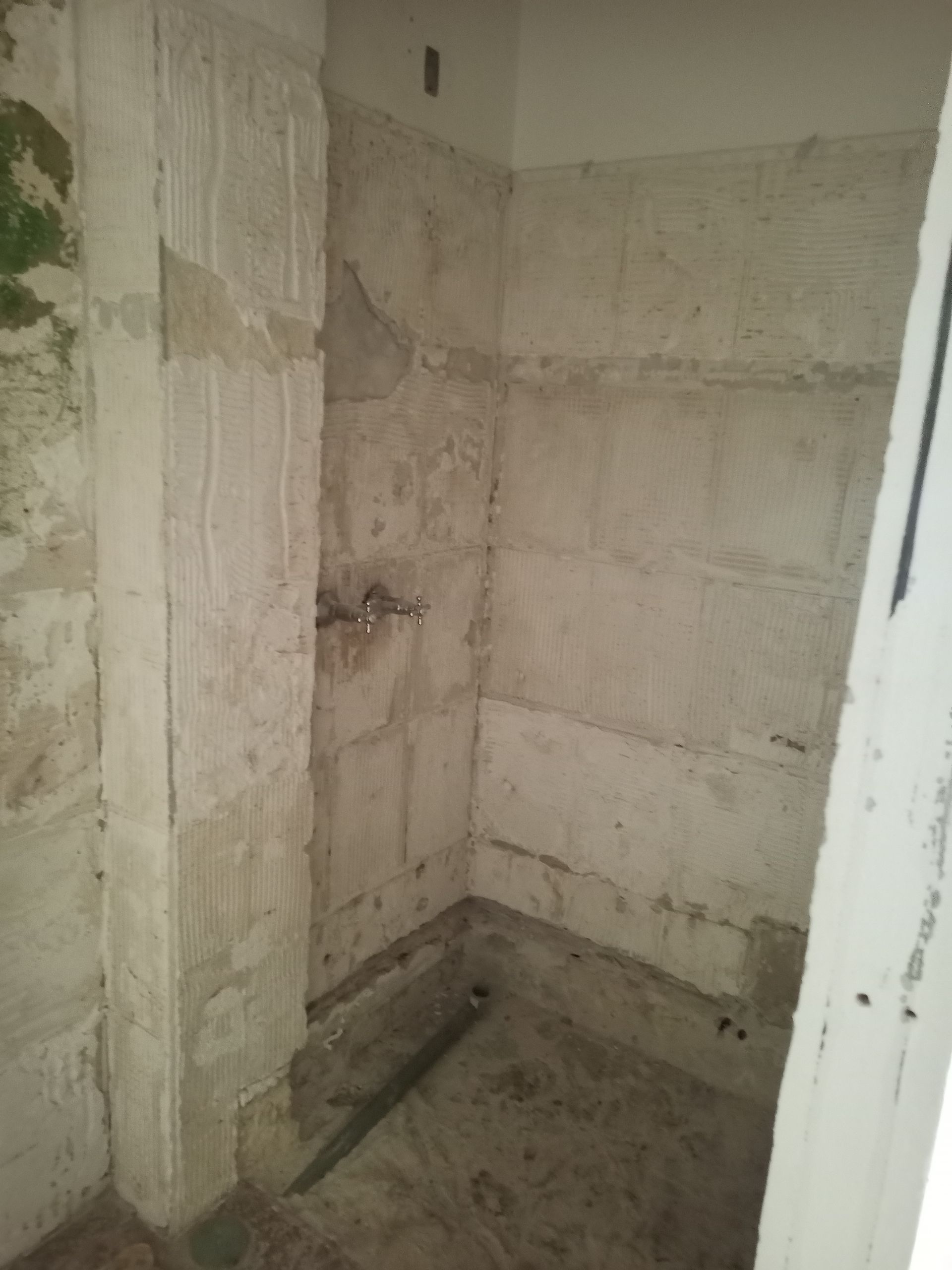 Box de chuveiro vazio e inacabado, com paredes e encanamento expostos.