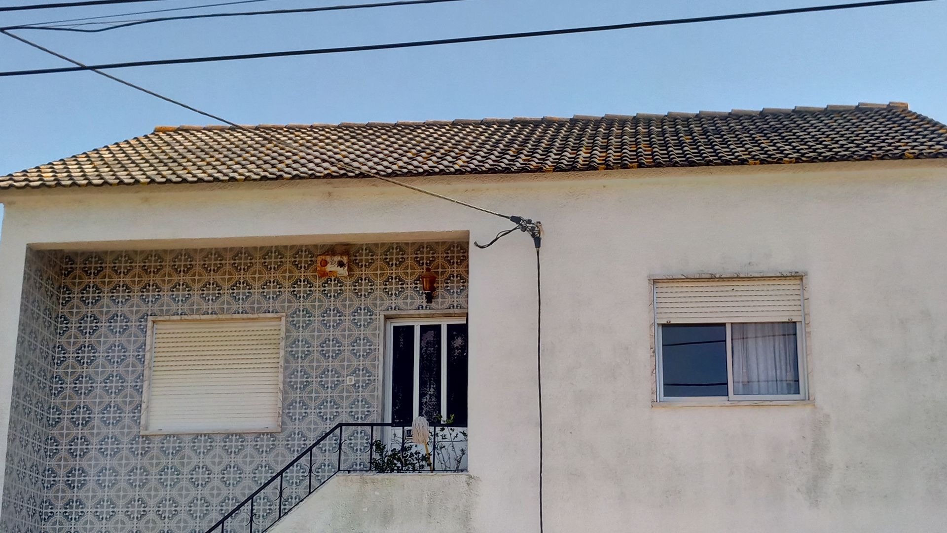 Casa de estuque branco com varanda frontal revestida de azulejos e janela fechada com persianas.