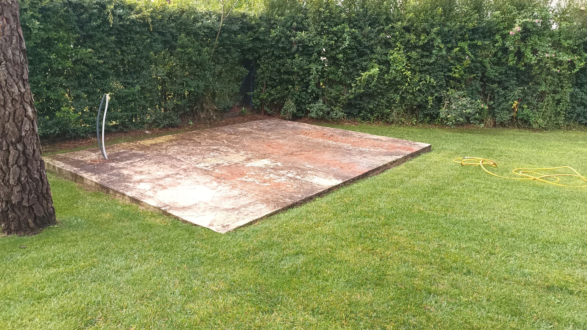 Plataforma de concreto com torneira em um gramado, cercada por uma sebe.