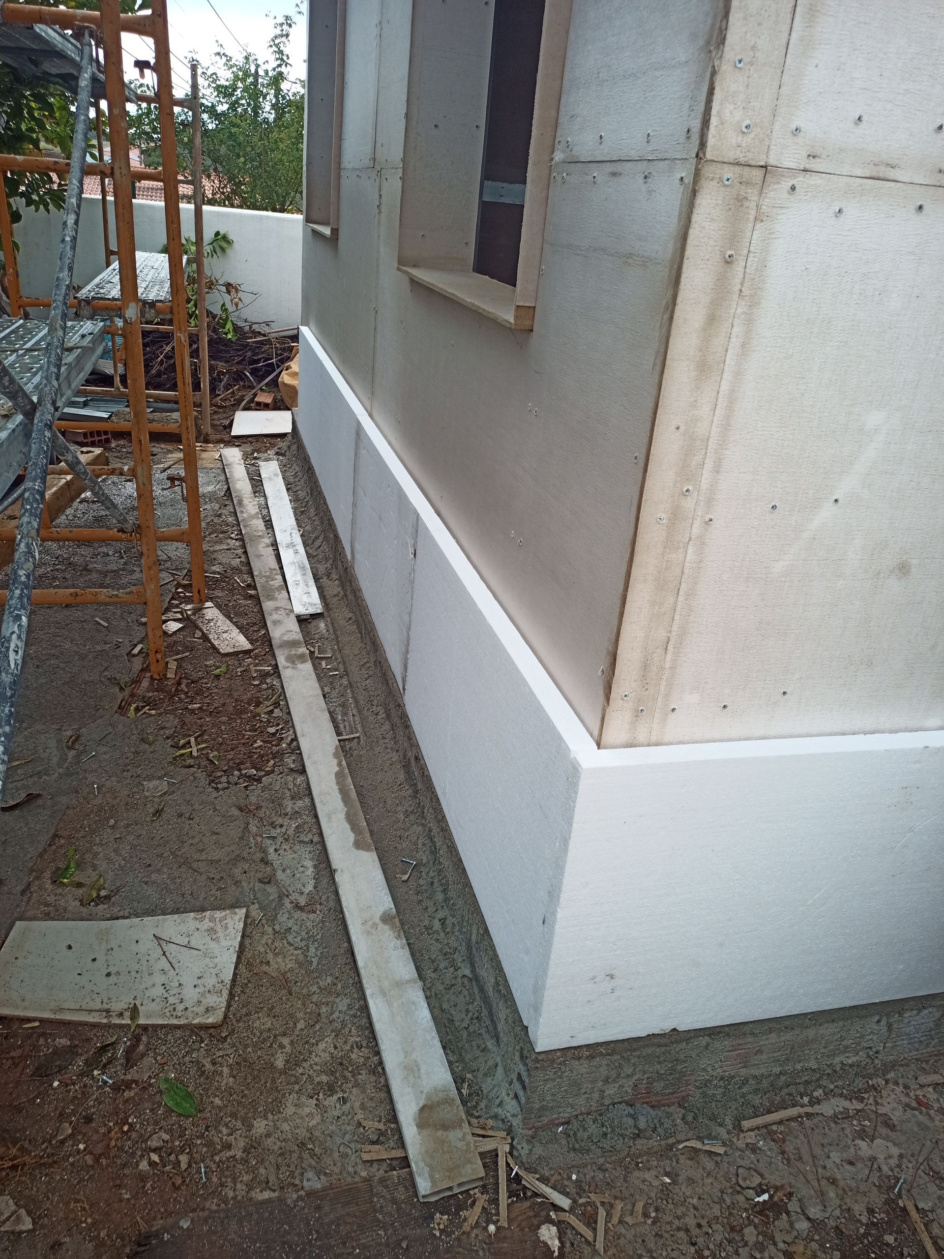 Construção da parede externa, com isolamento de espuma branca na base e uma vala estreita. Os andaimes são parcialmente visíveis.
