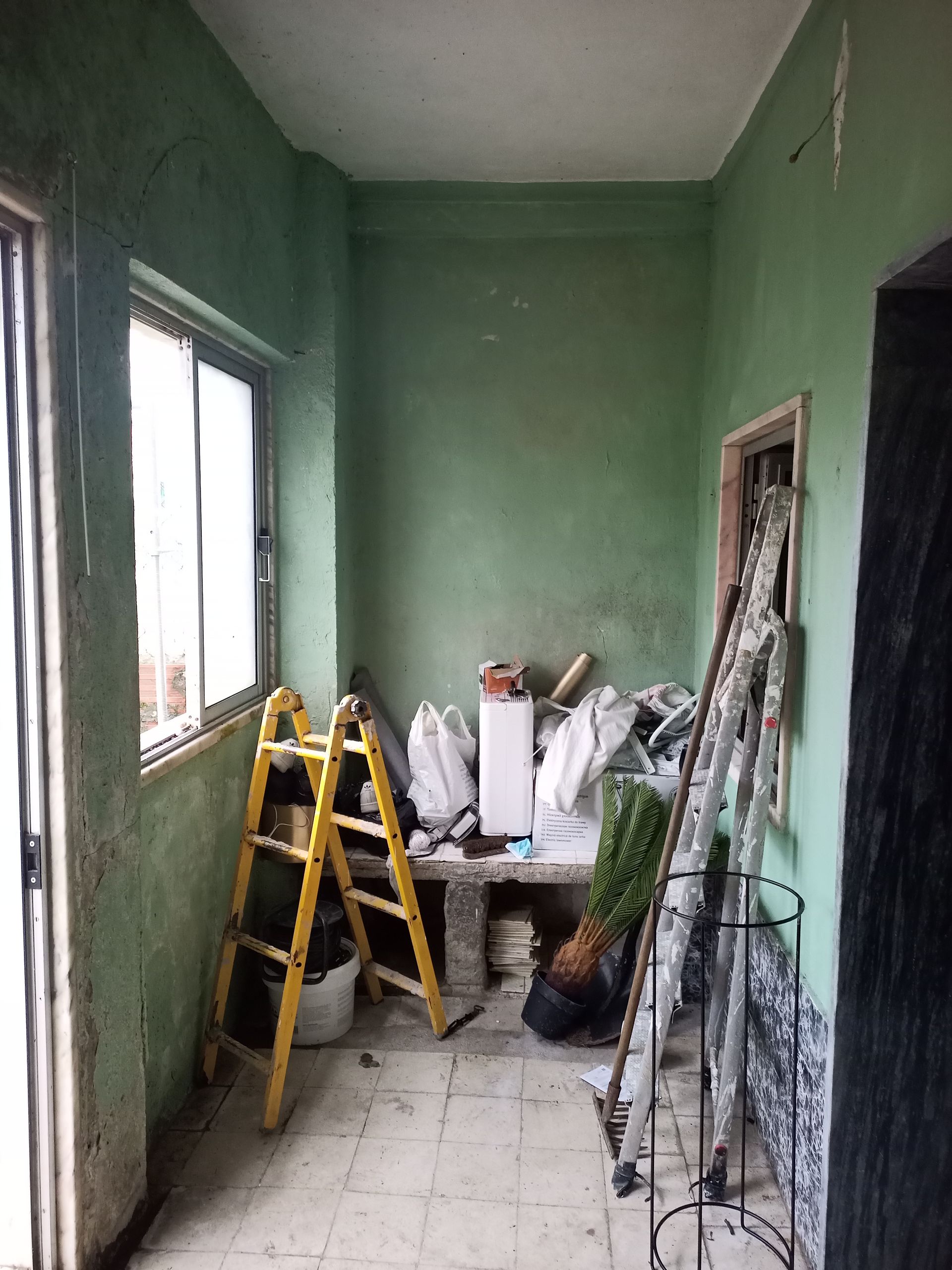 Sala verde com janela, escada amarela e diversos objetos guardados contra as paredes.