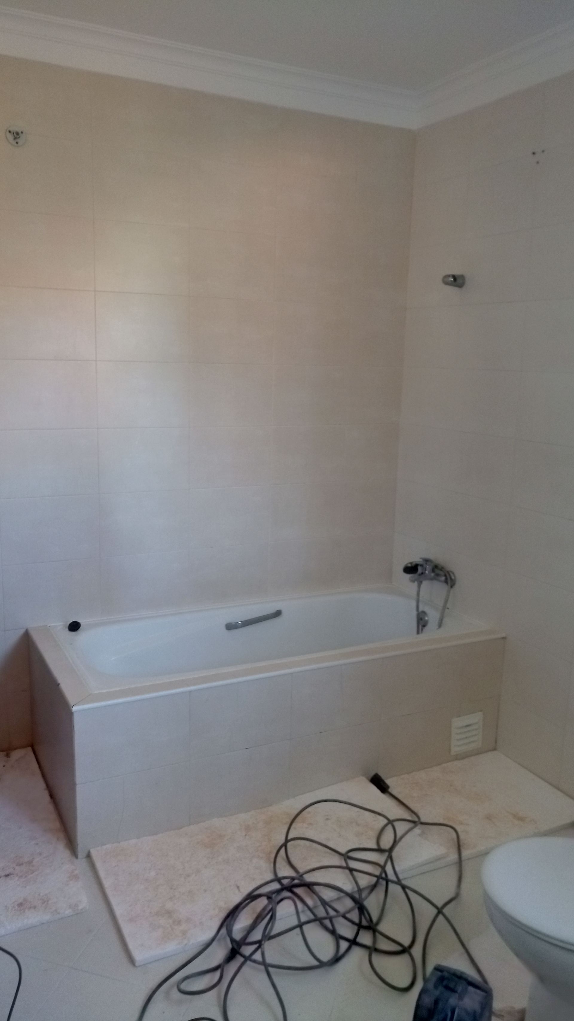 Banheiro em construção, com banheira, azulejos bege e fiação elétrica.
